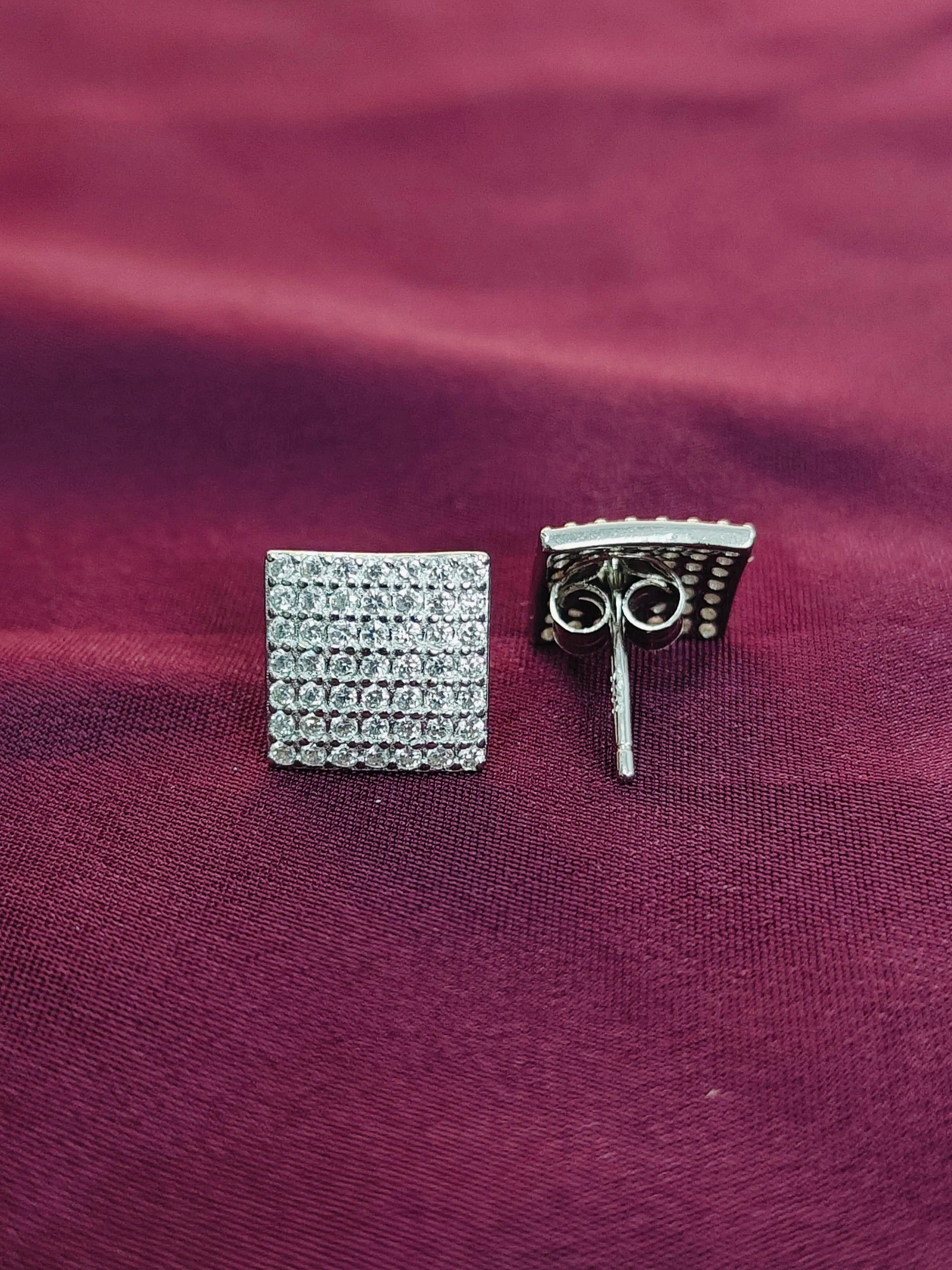 Two silver earrings on a purple fabric background