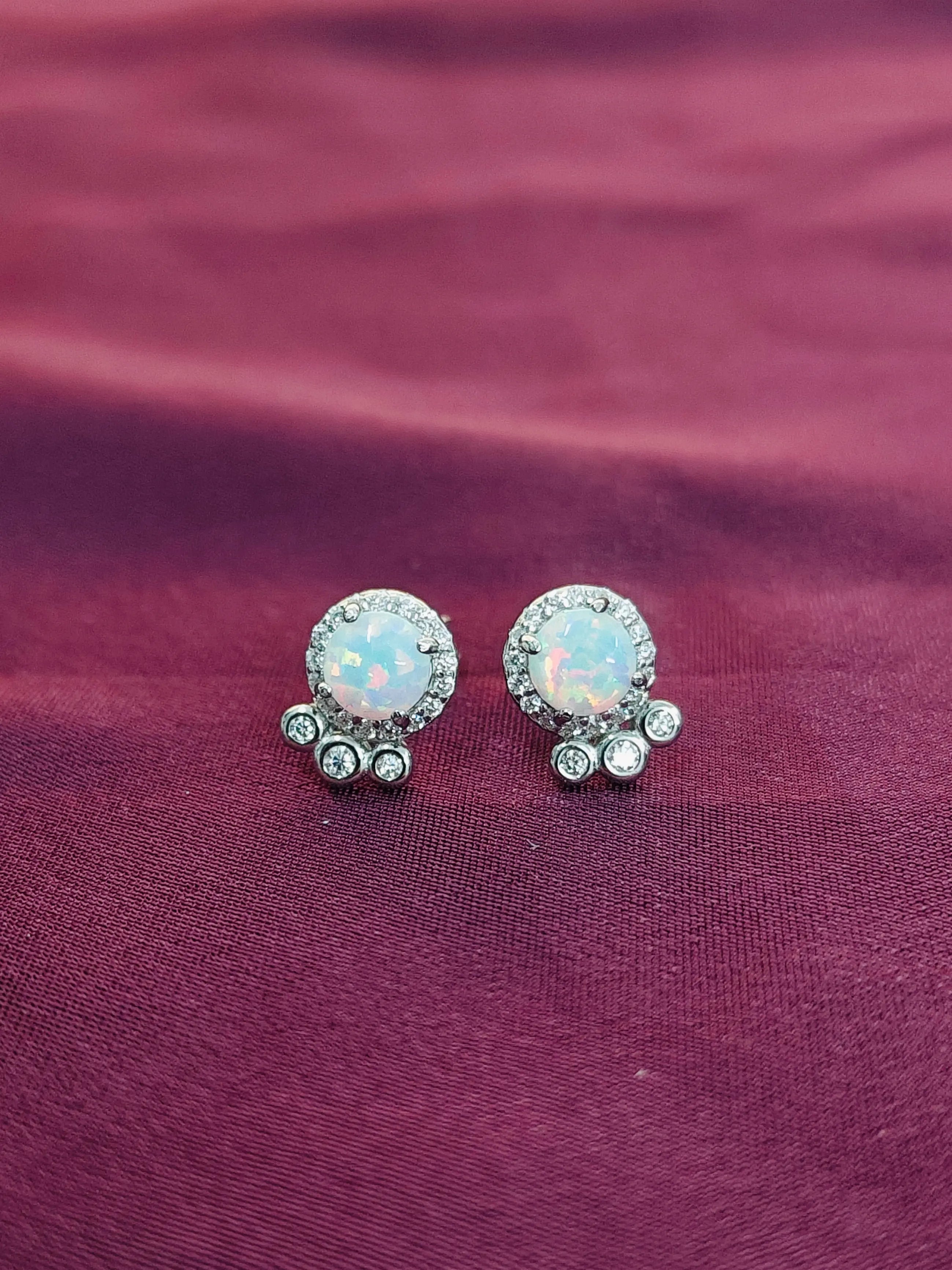 Pair of silver earrings with opal-like stones on a maroon fabric background