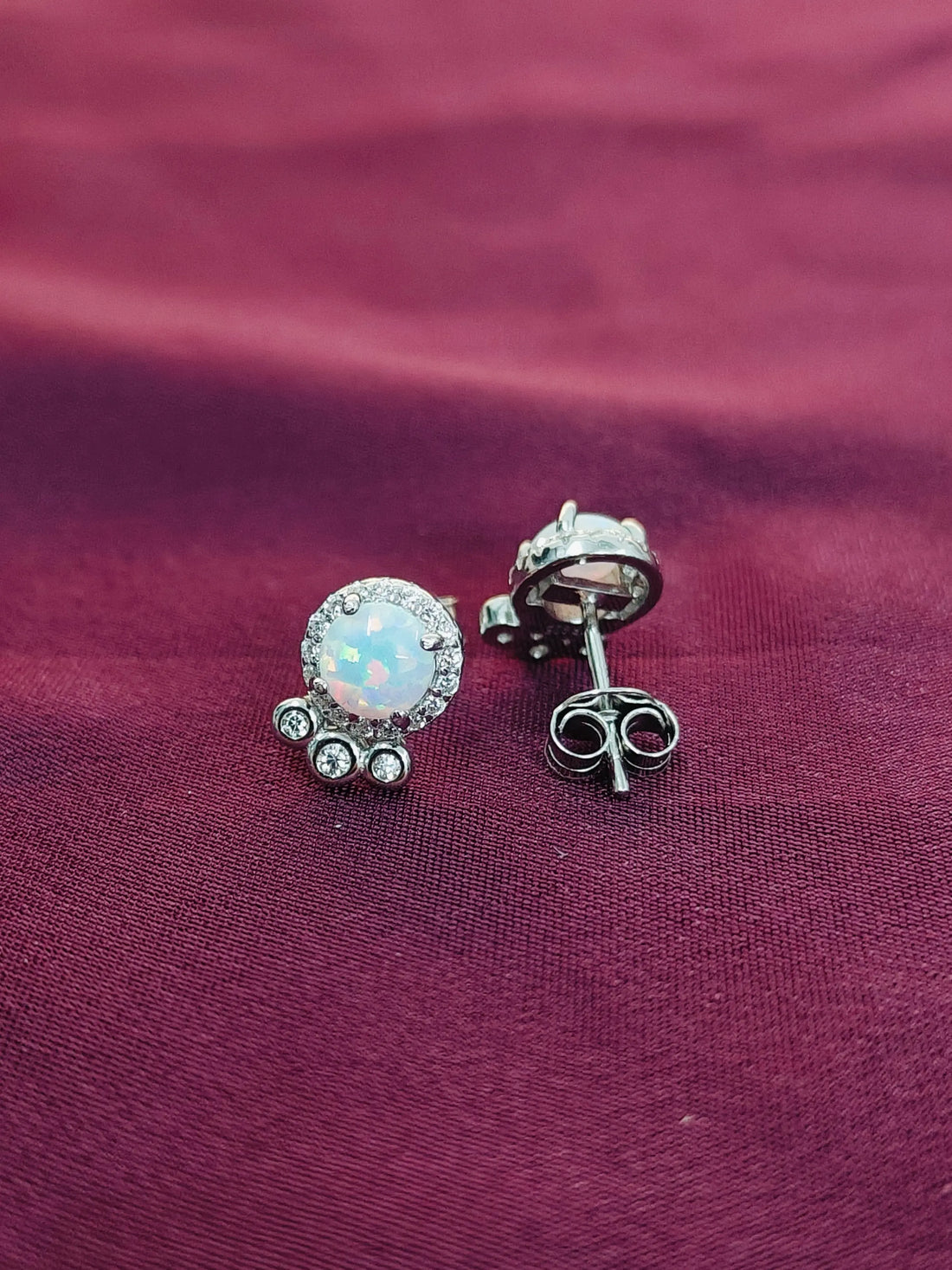 Pair of silver earrings with a central gemstone on a purple fabric background