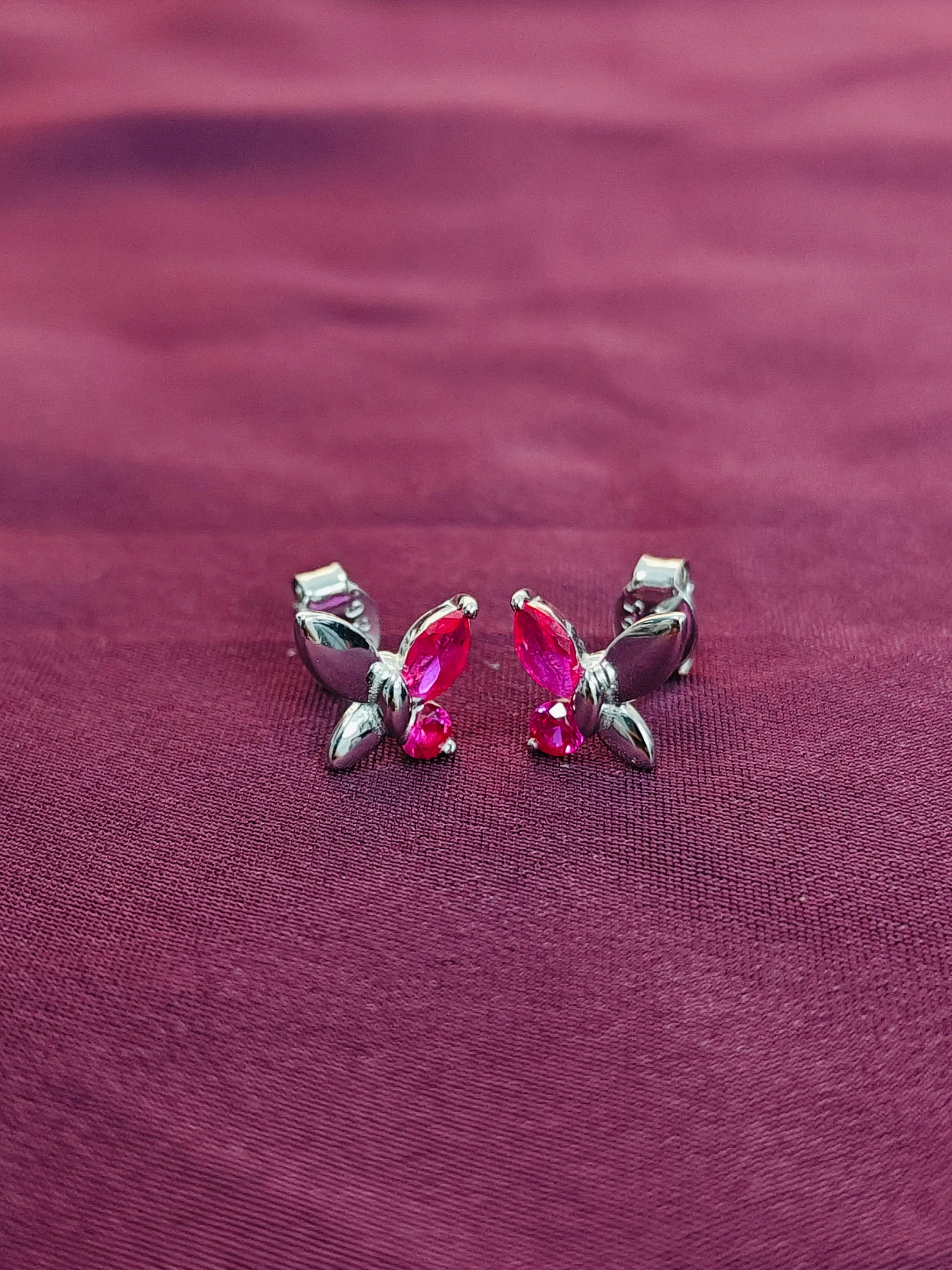 Butterfly-shaped earrings with pink gemstones on a purple fabric background