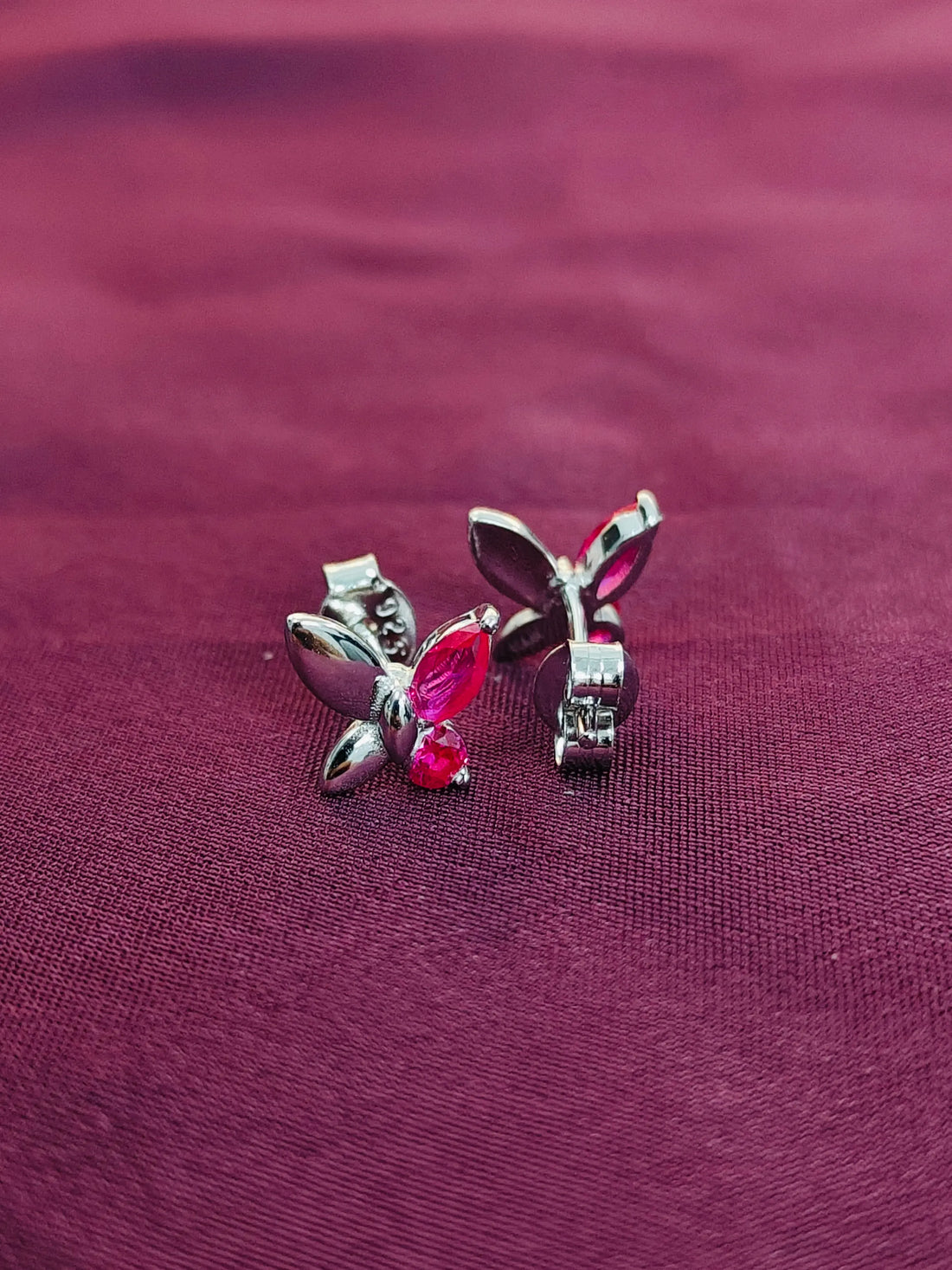 Butterfly-shaped earrings with red gemstones on a purple fabric background