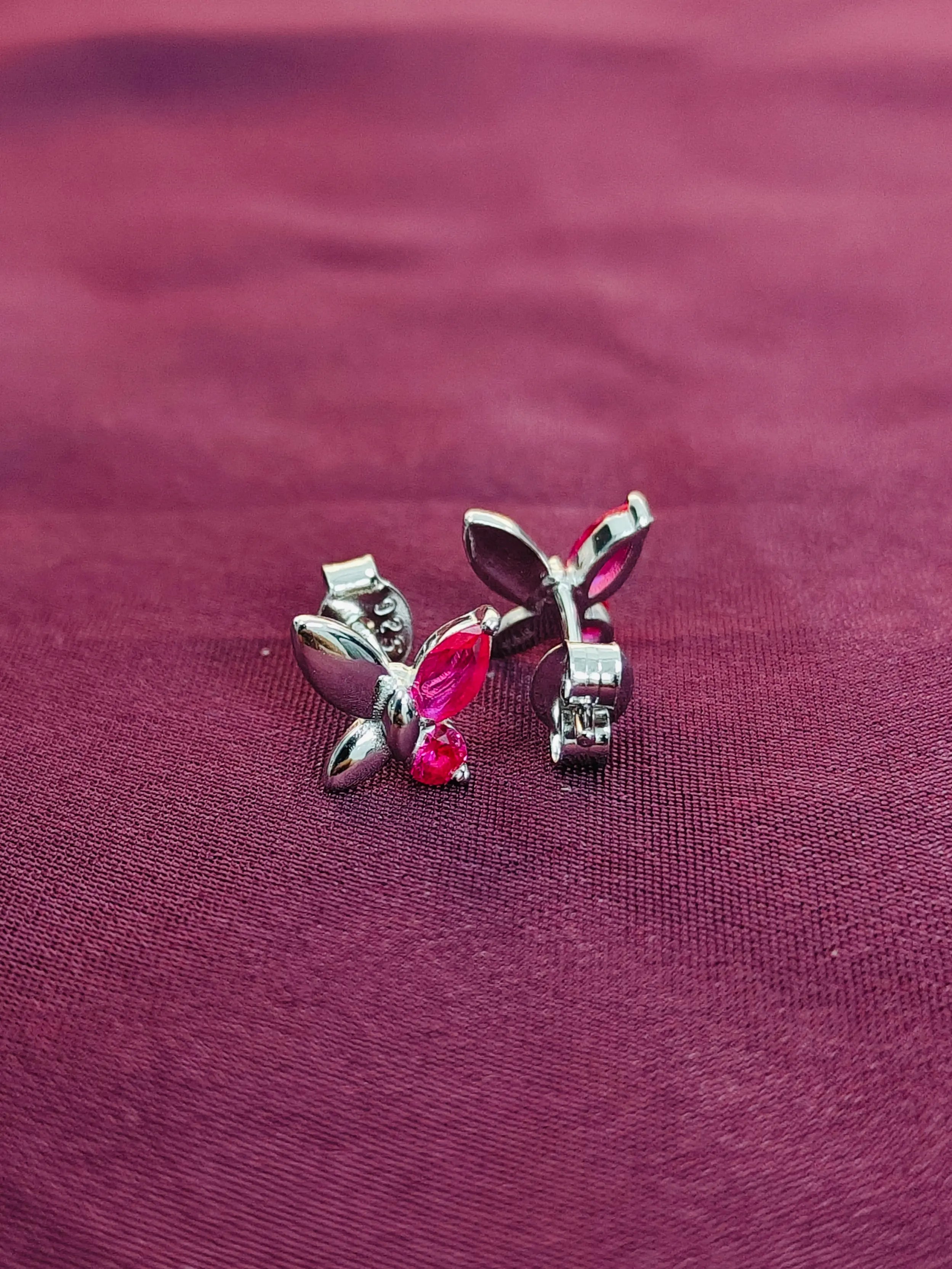 Butterfly-shaped earrings with red gemstones on a maroon fabric background
