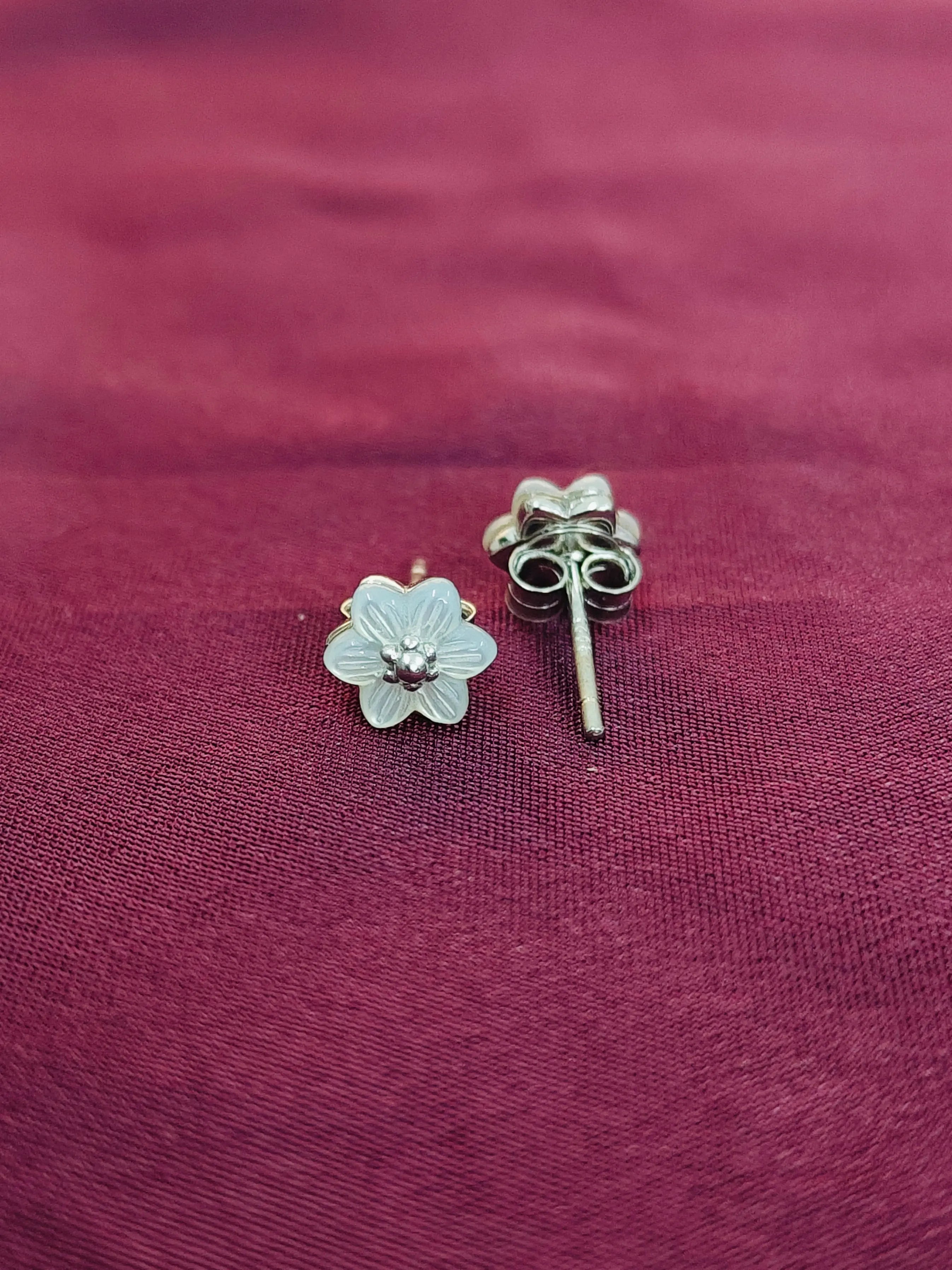 Silver flower-shaped earrings on a maroon fabric background