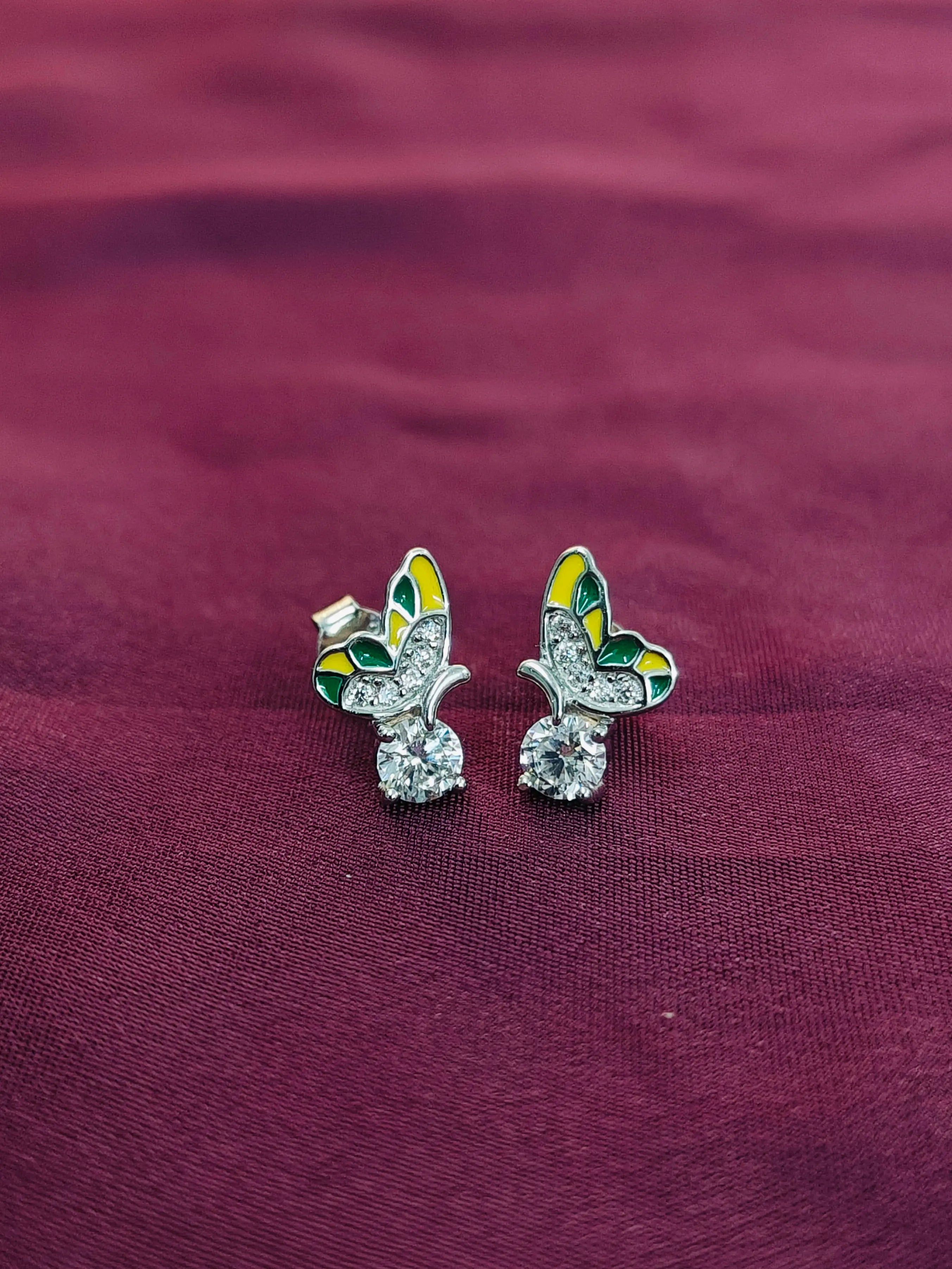 Butterfly-shaped earrings with green and yellow details on a purple fabric background