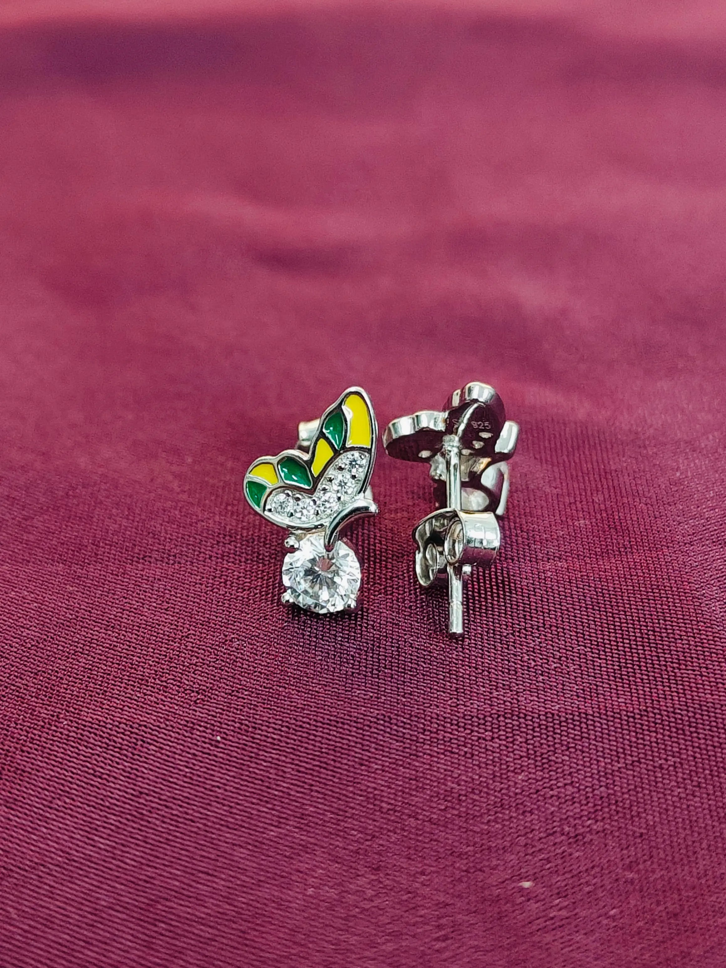 Butterfly-shaped earrings with gemstones on a maroon fabric background