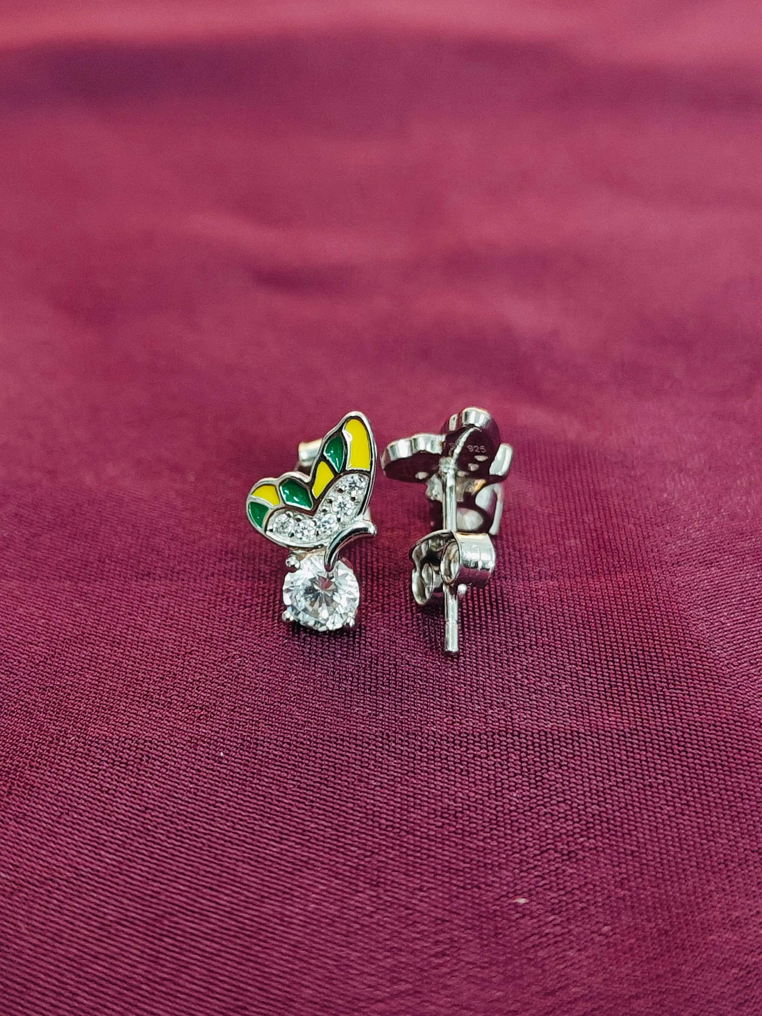 Butterfly-shaped earrings on a maroon fabric background