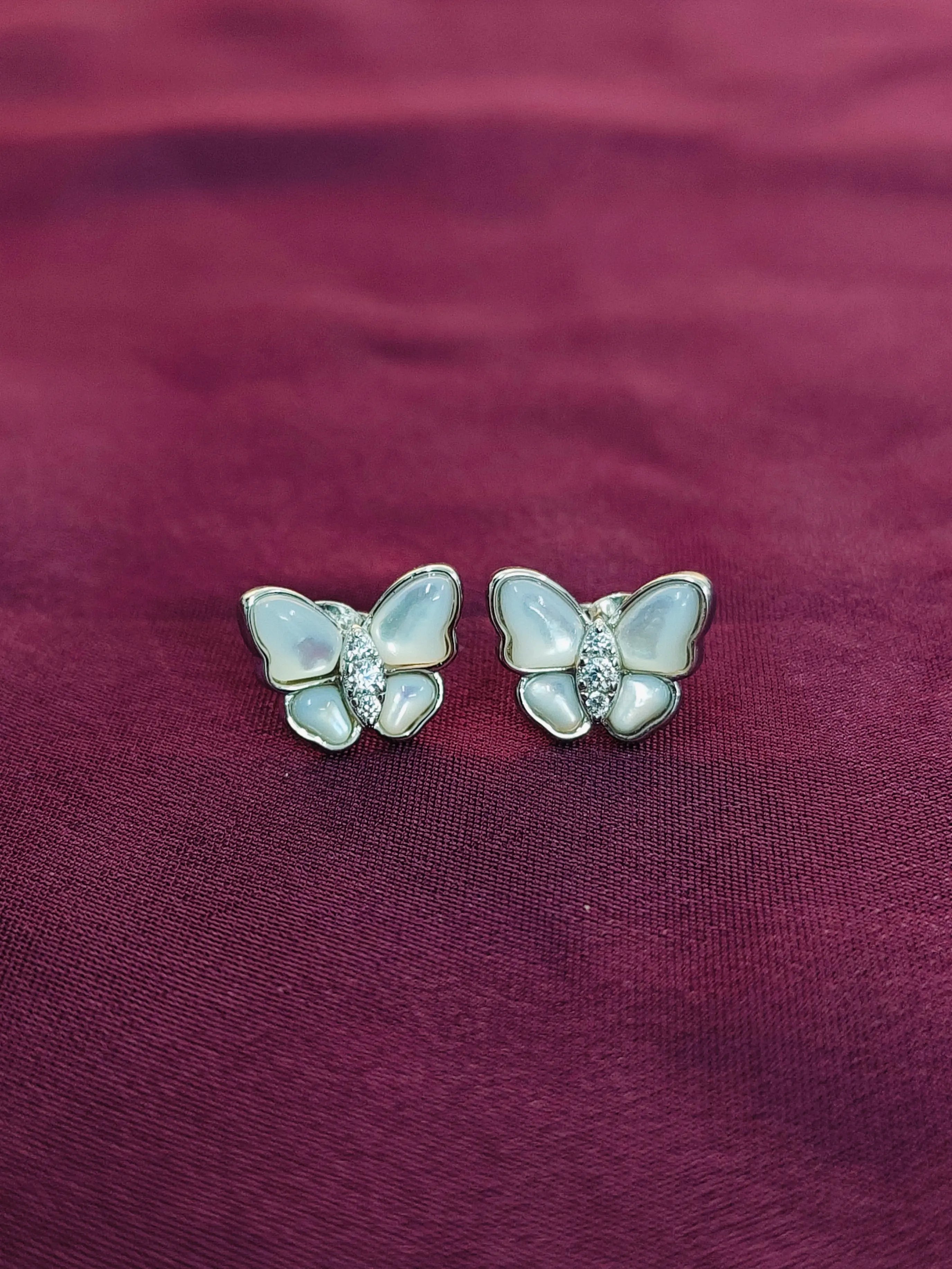 Butterfly-shaped earrings with gemstones on a maroon fabric background