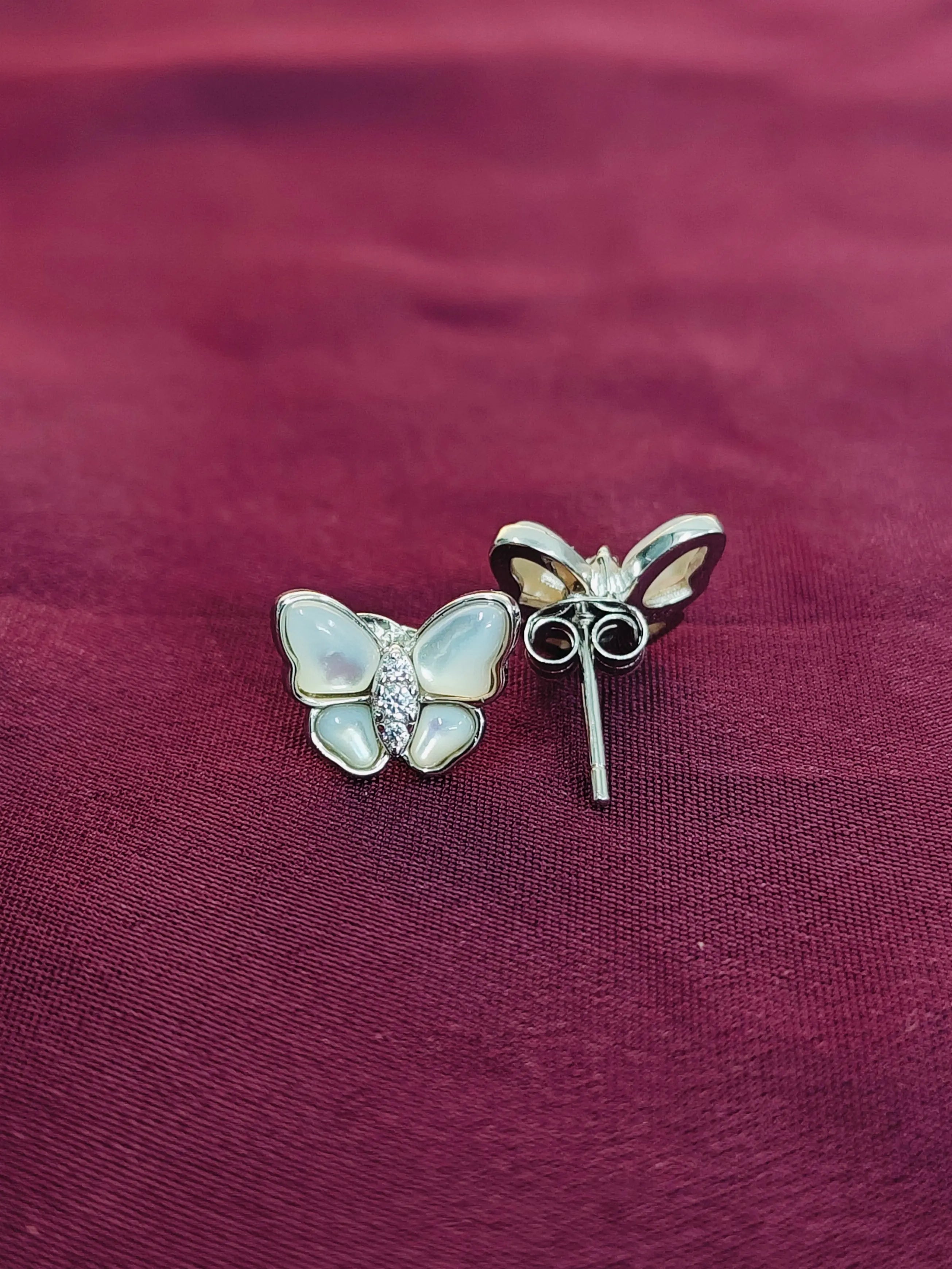 Butterfly-shaped earrings on a maroon fabric background