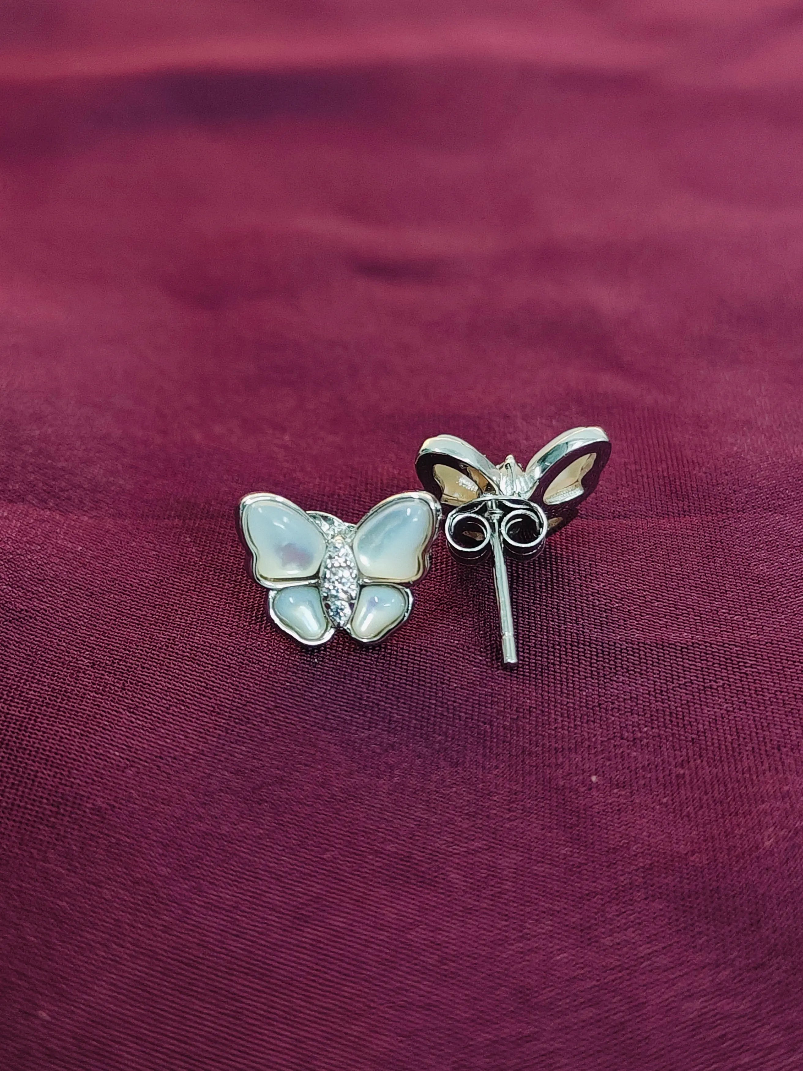 Butterfly-shaped earrings on a maroon fabric background