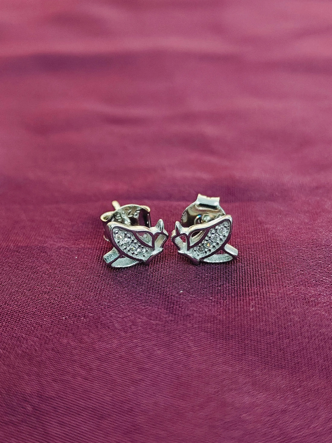 Silver owl-shaped earrings on a maroon fabric background