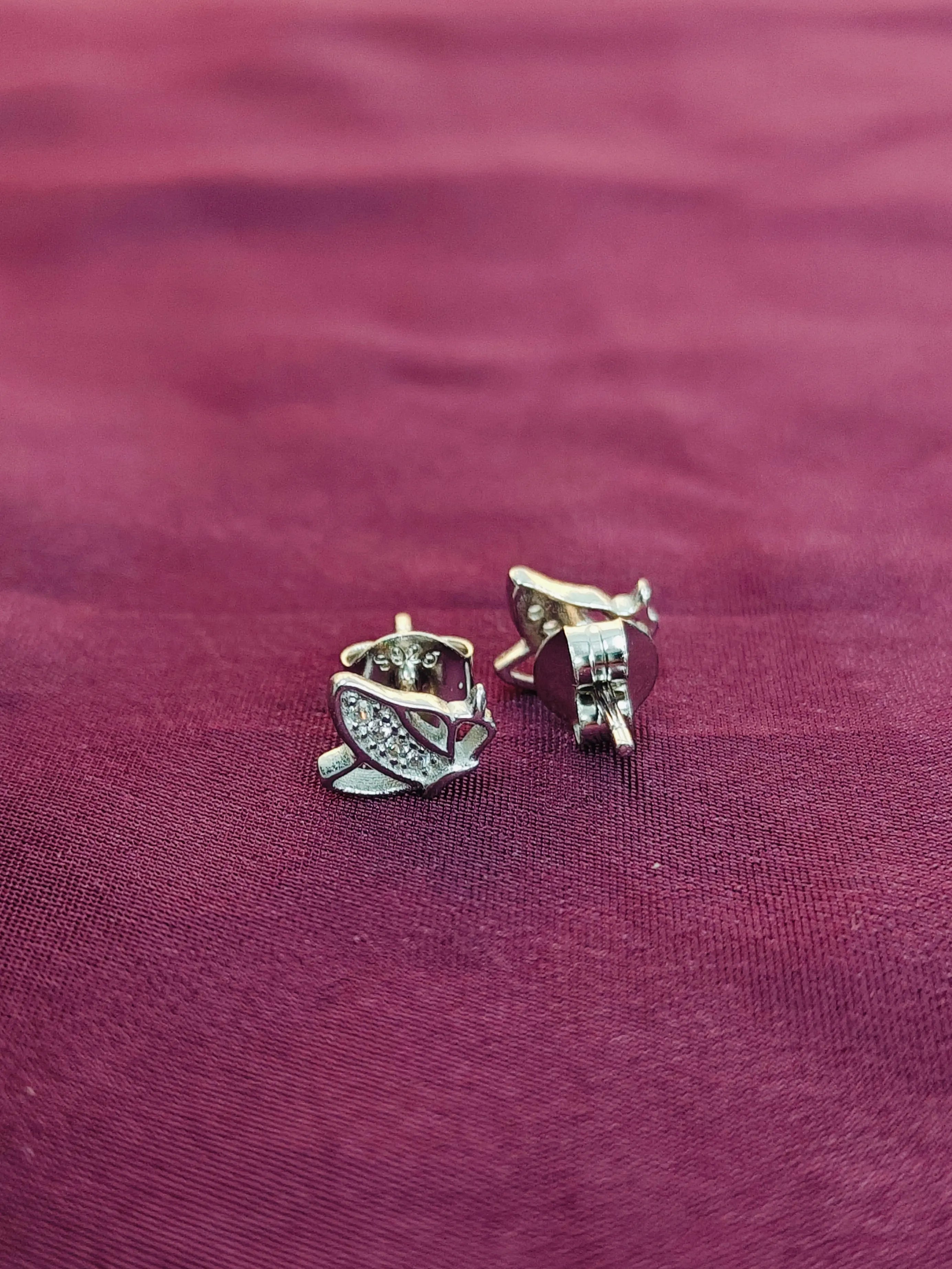 Silver earrings on a maroon fabric background