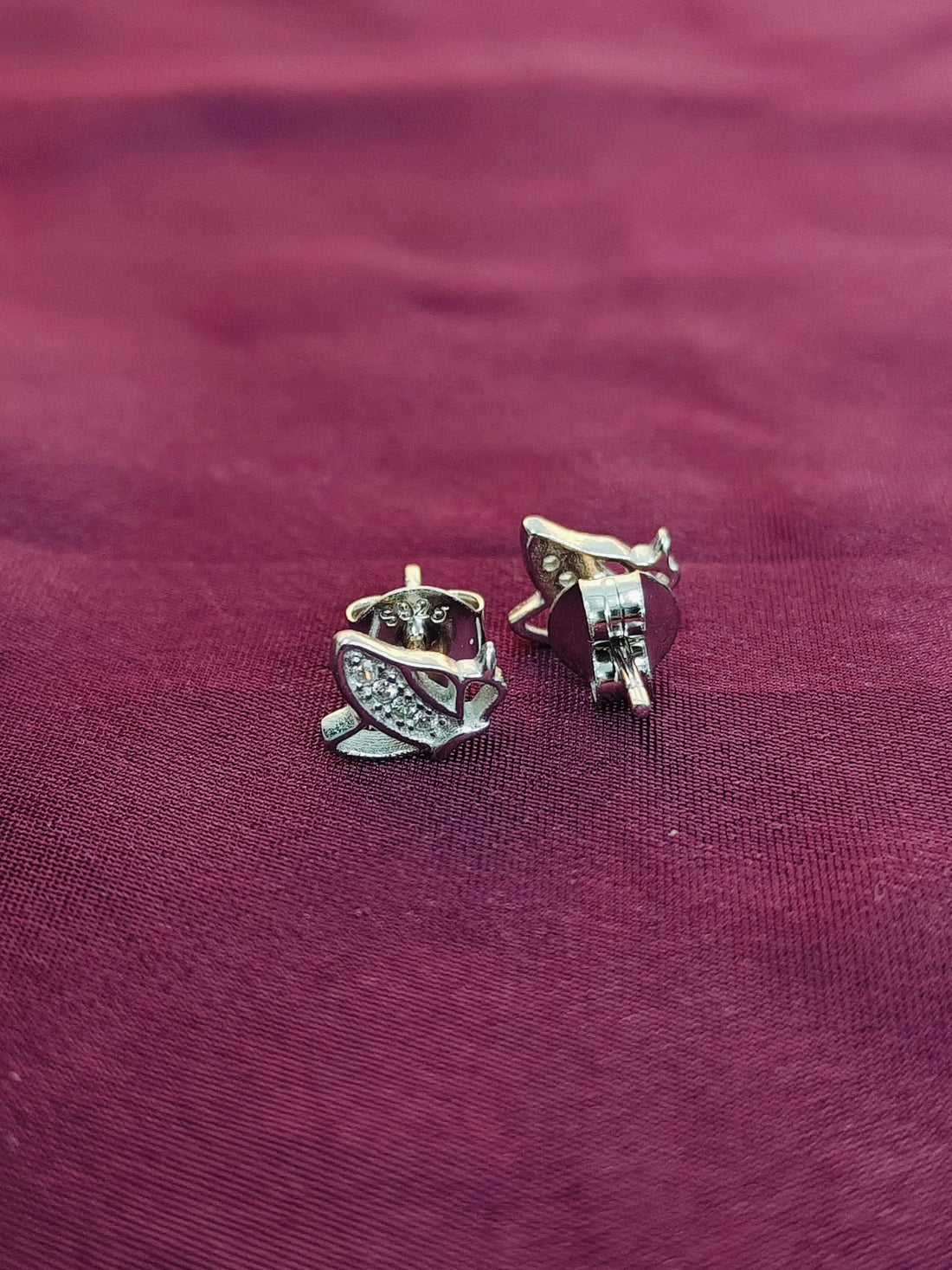 Silver earrings on a maroon fabric background