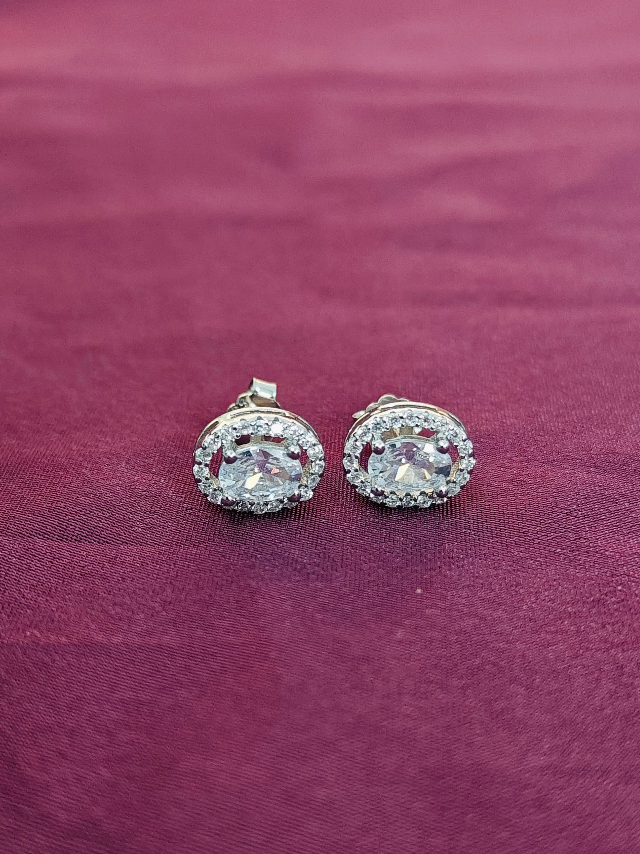 Pair of silver earrings with clear stones on a purple fabric background
