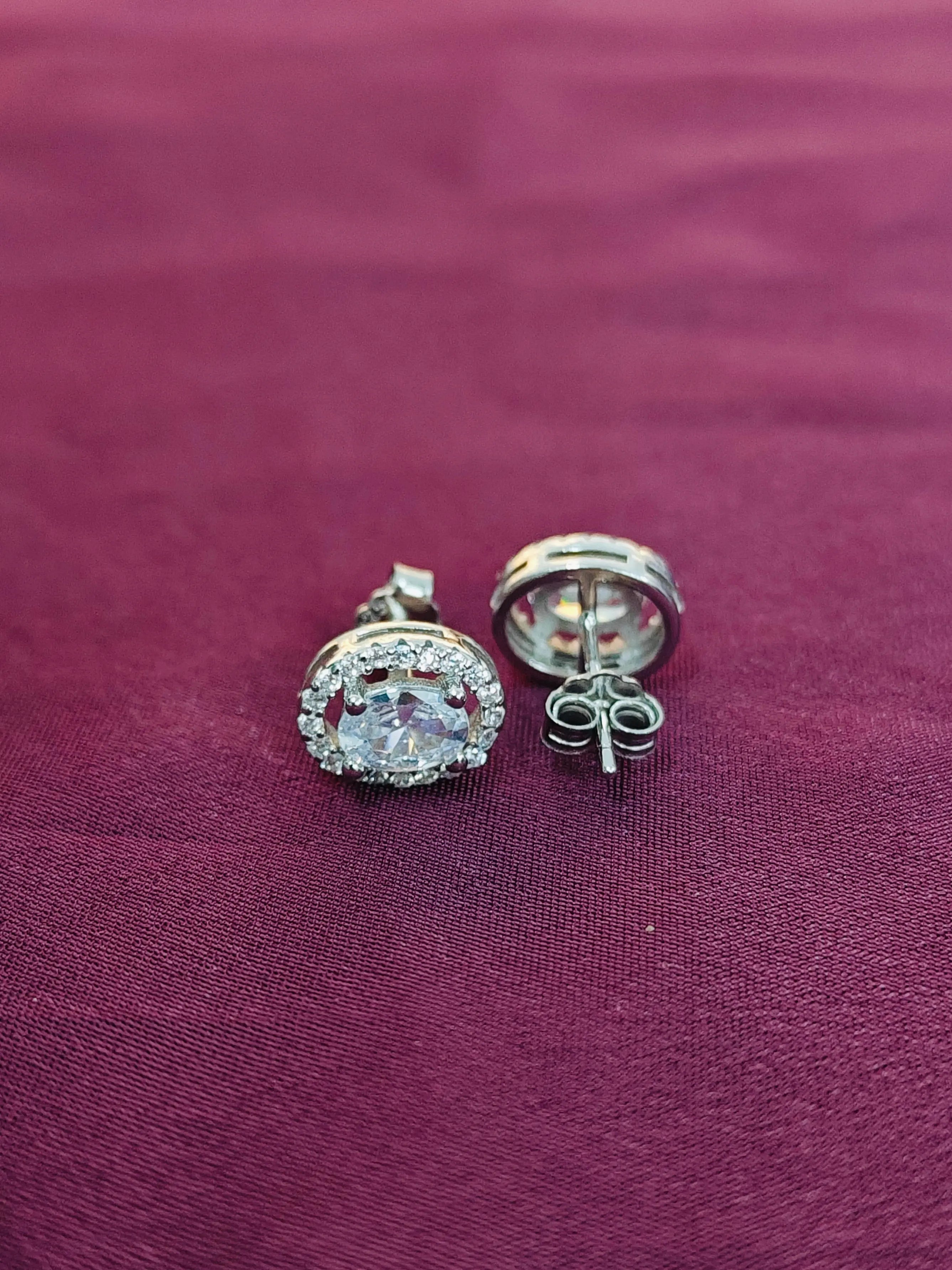 Silver earrings with a clear gemstone on a purple fabric background