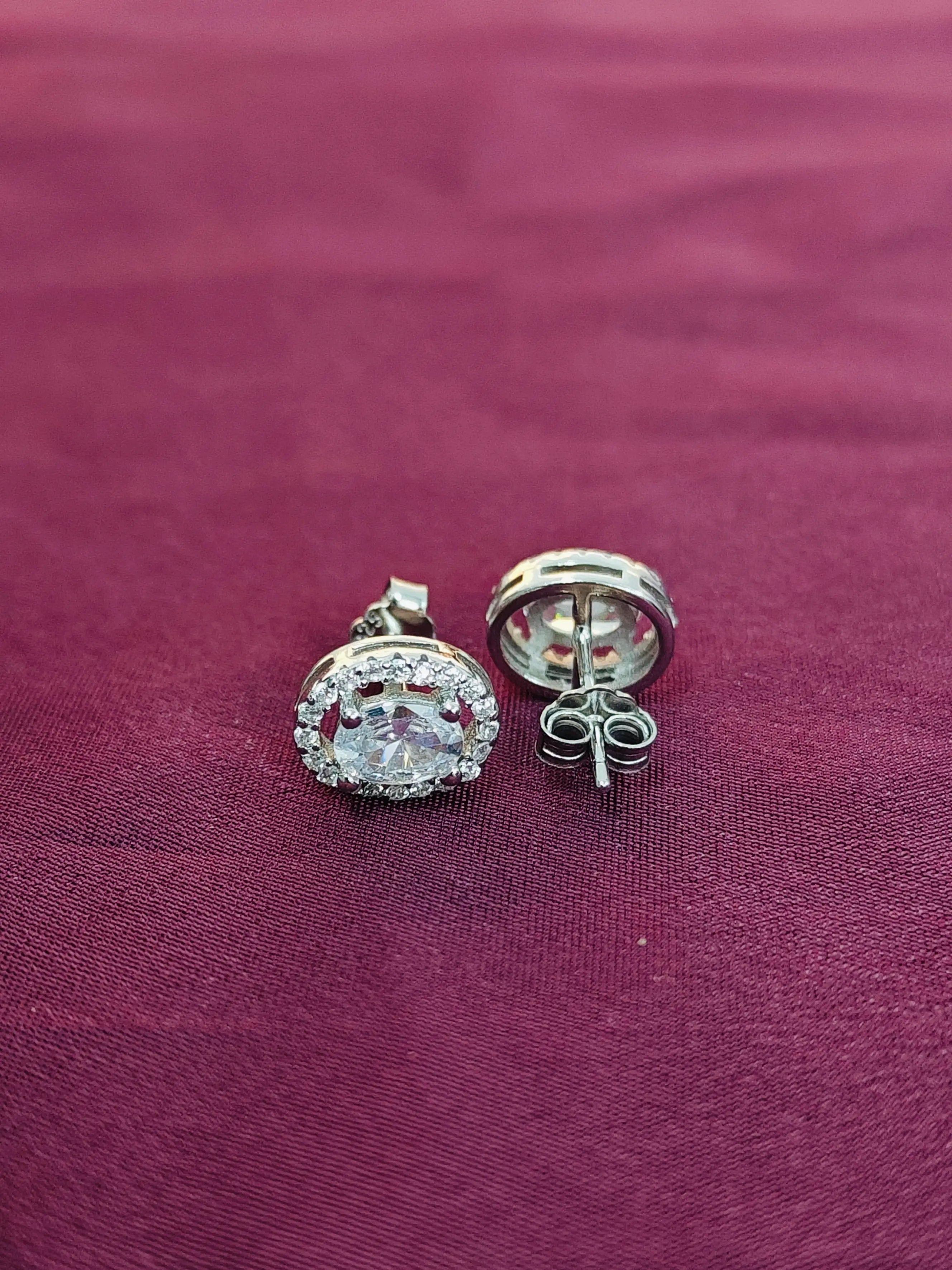 Silver earrings with clear gemstones on a maroon fabric background