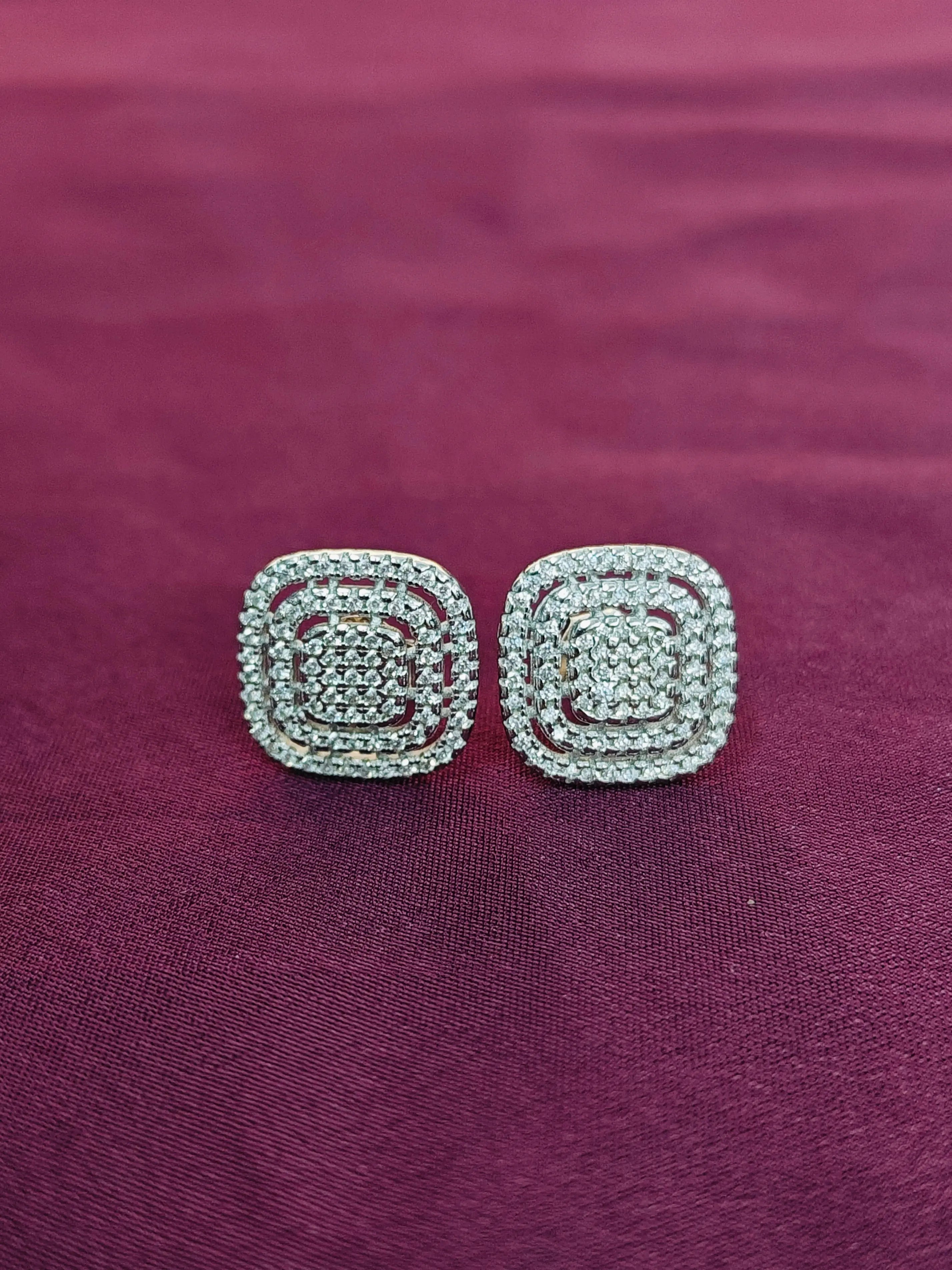 Pair of silver square earrings on a purple fabric background