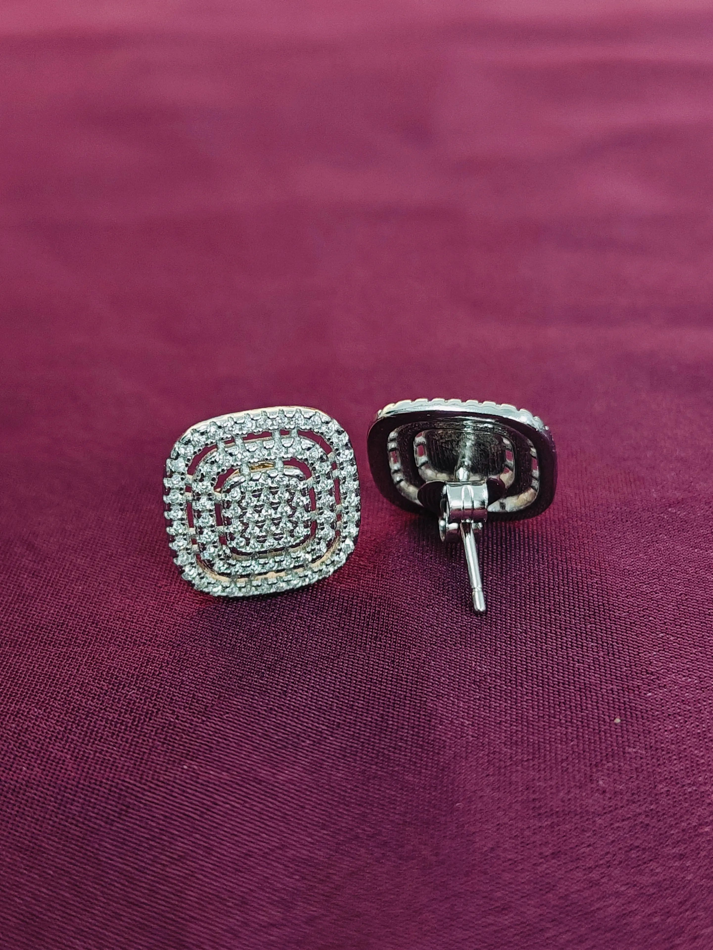 Silver square-shaped earring with clear stones on a purple fabric background