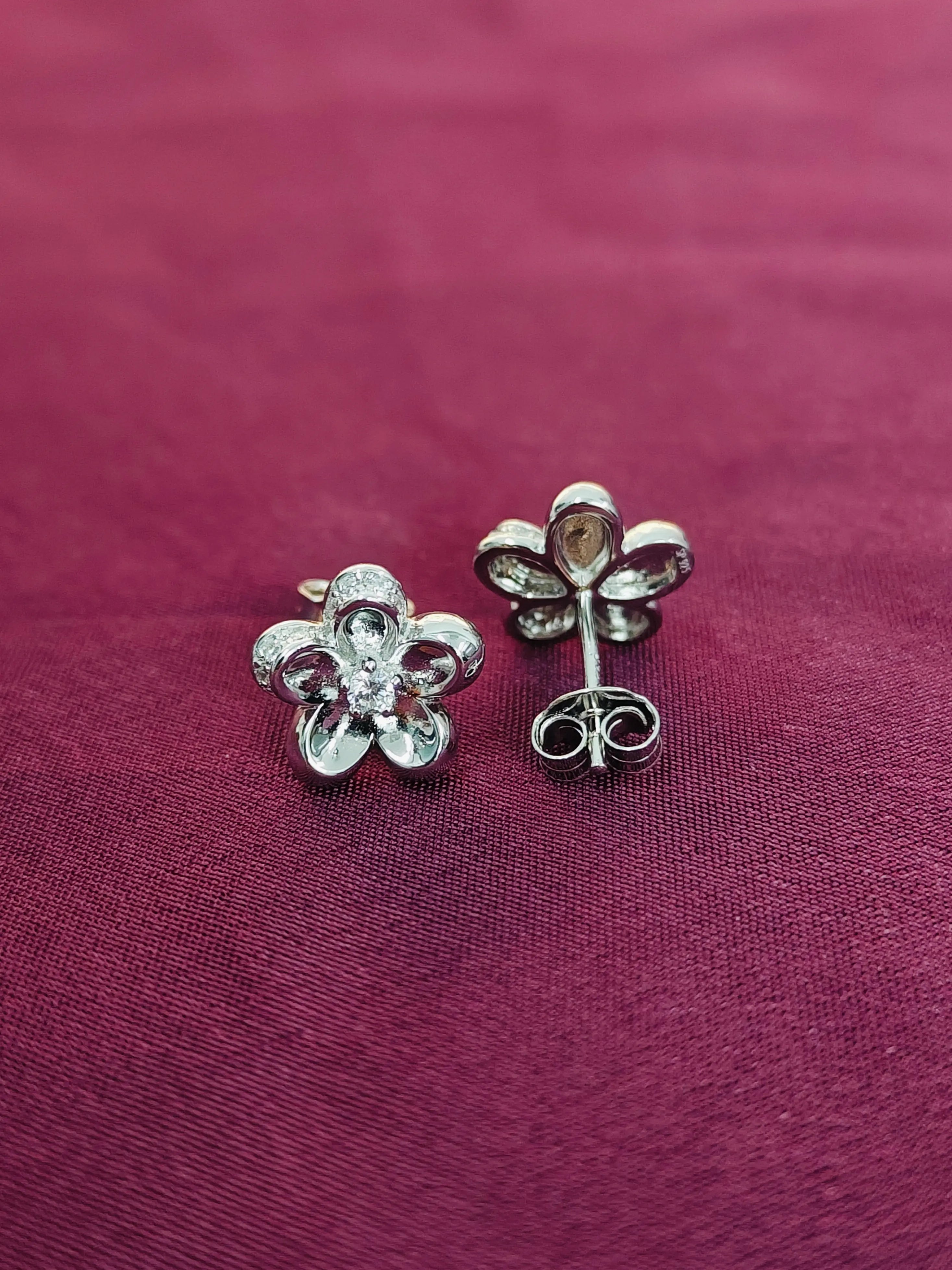 Flower-shaped silver earrings on a maroon fabric background