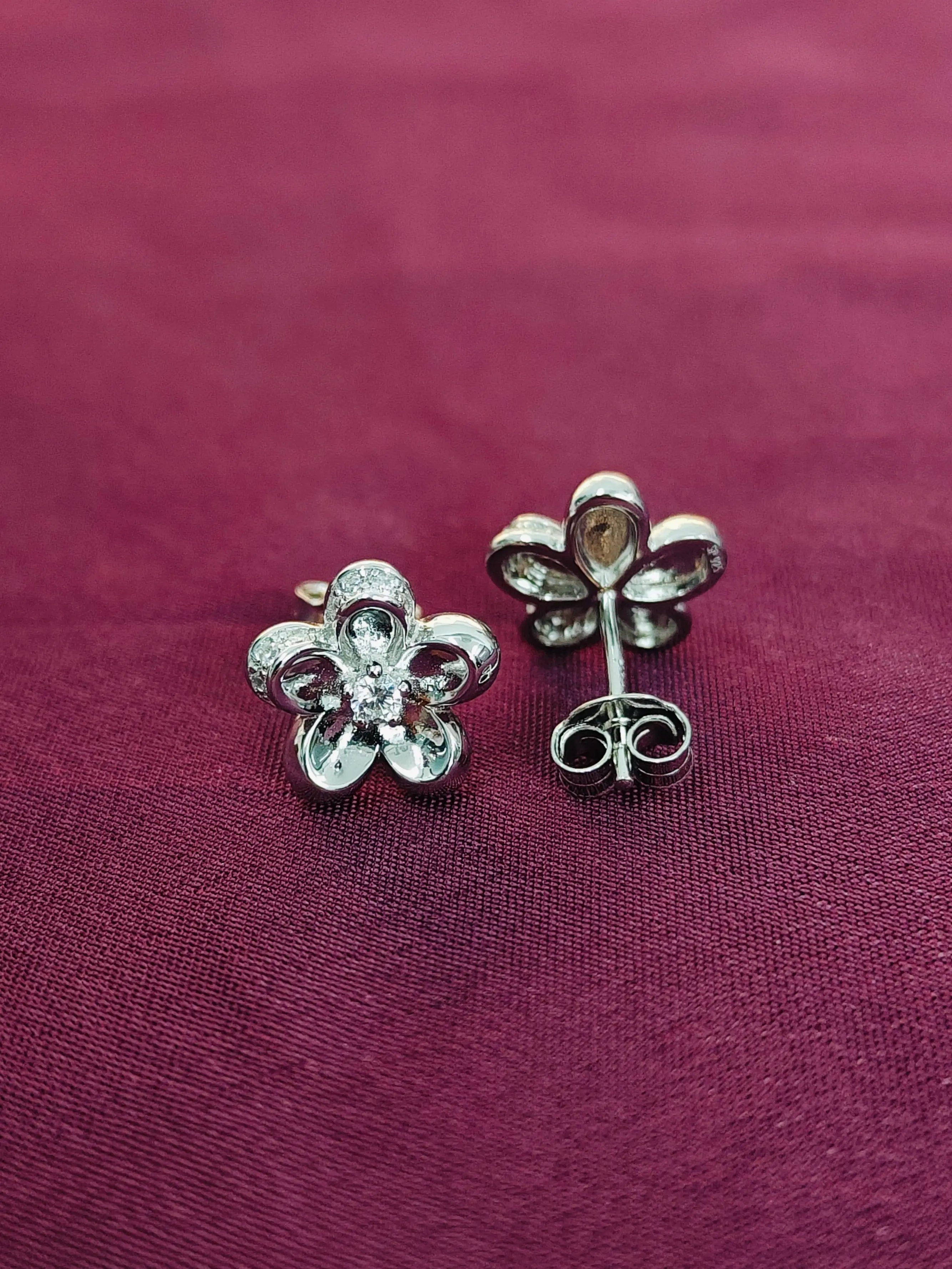 Flower-shaped silver earrings on a purple fabric background