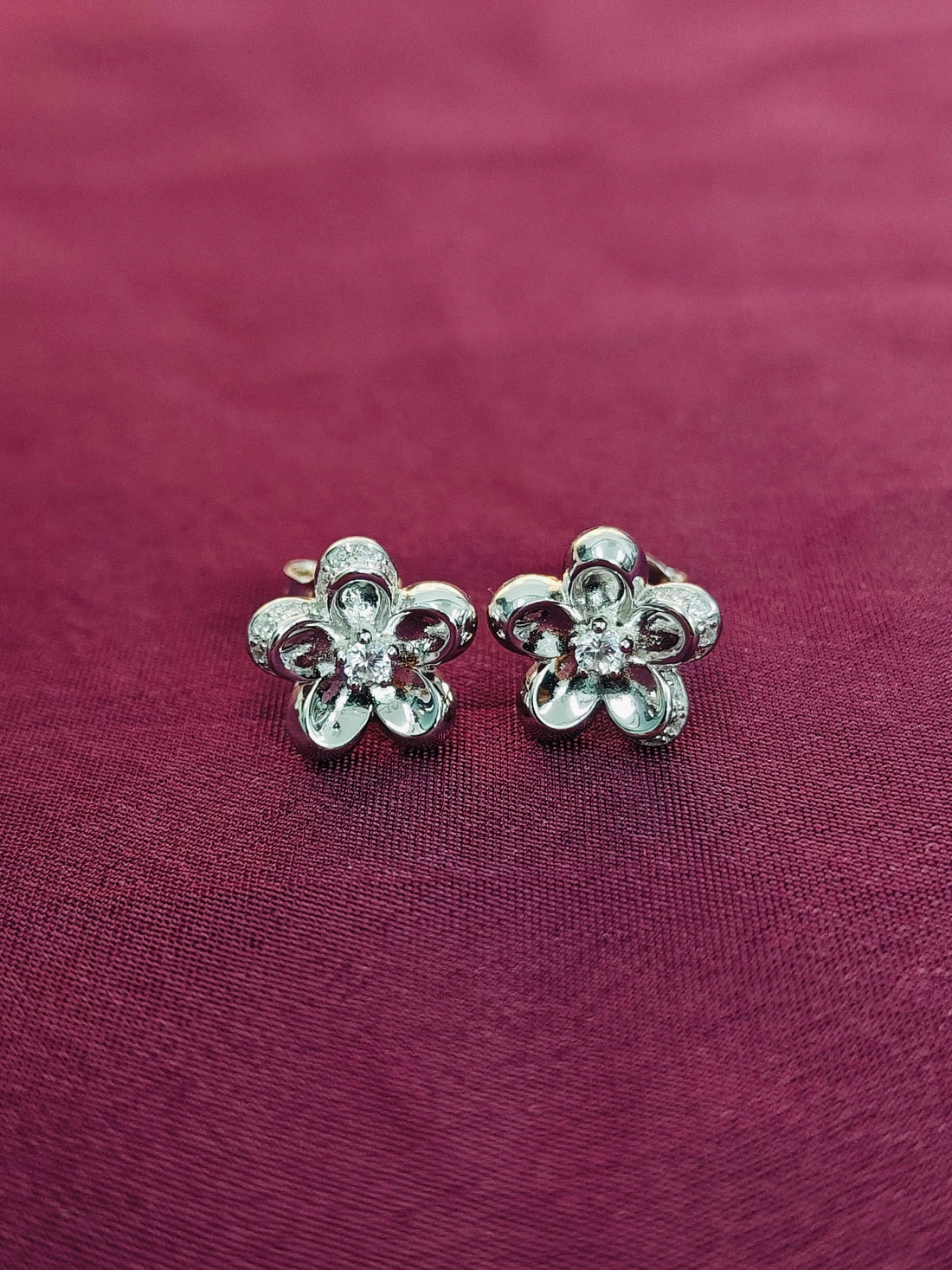 Silver flower-shaped earrings on a maroon fabric background