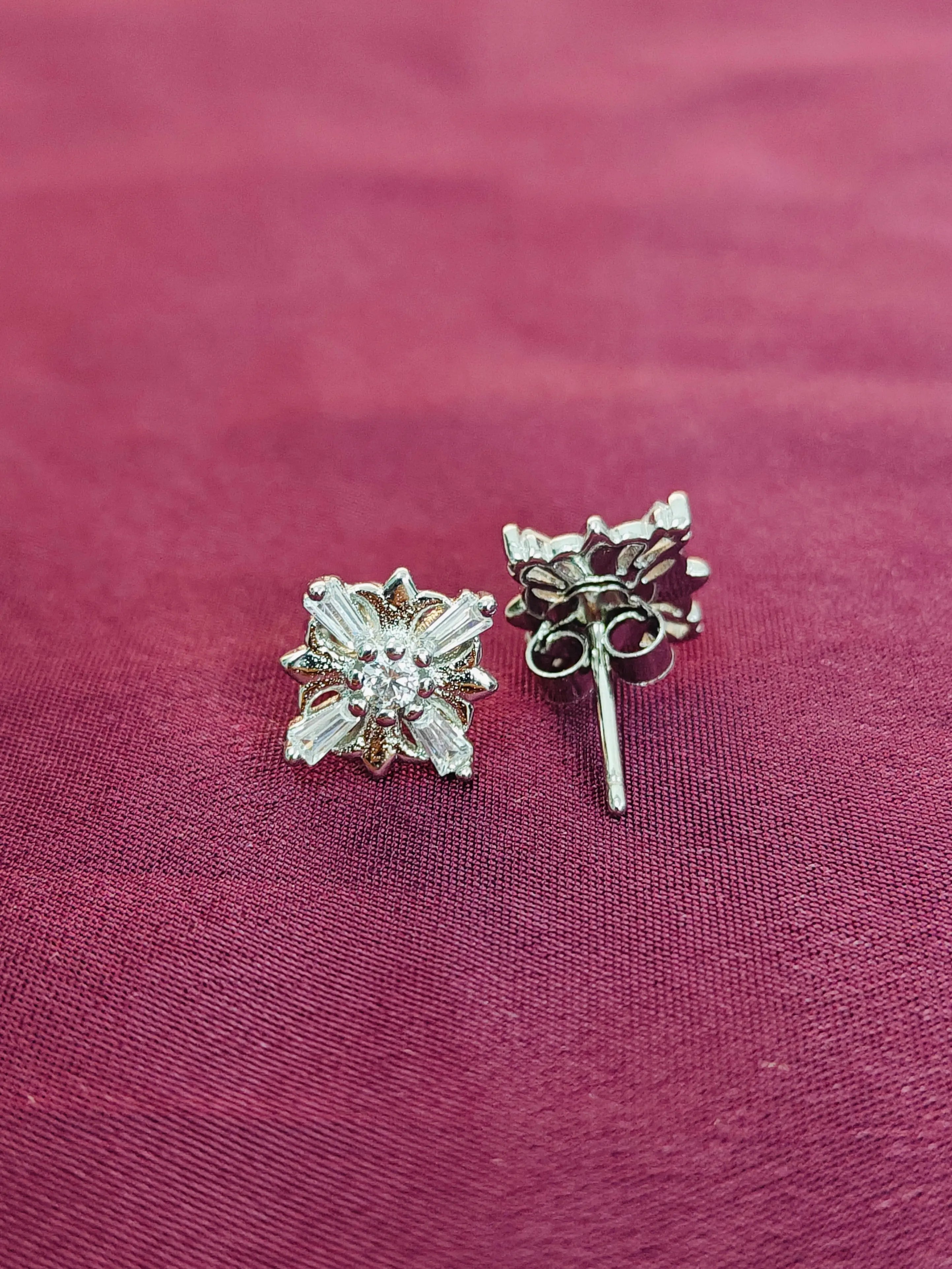 Pair of silver earrings on a maroon fabric background