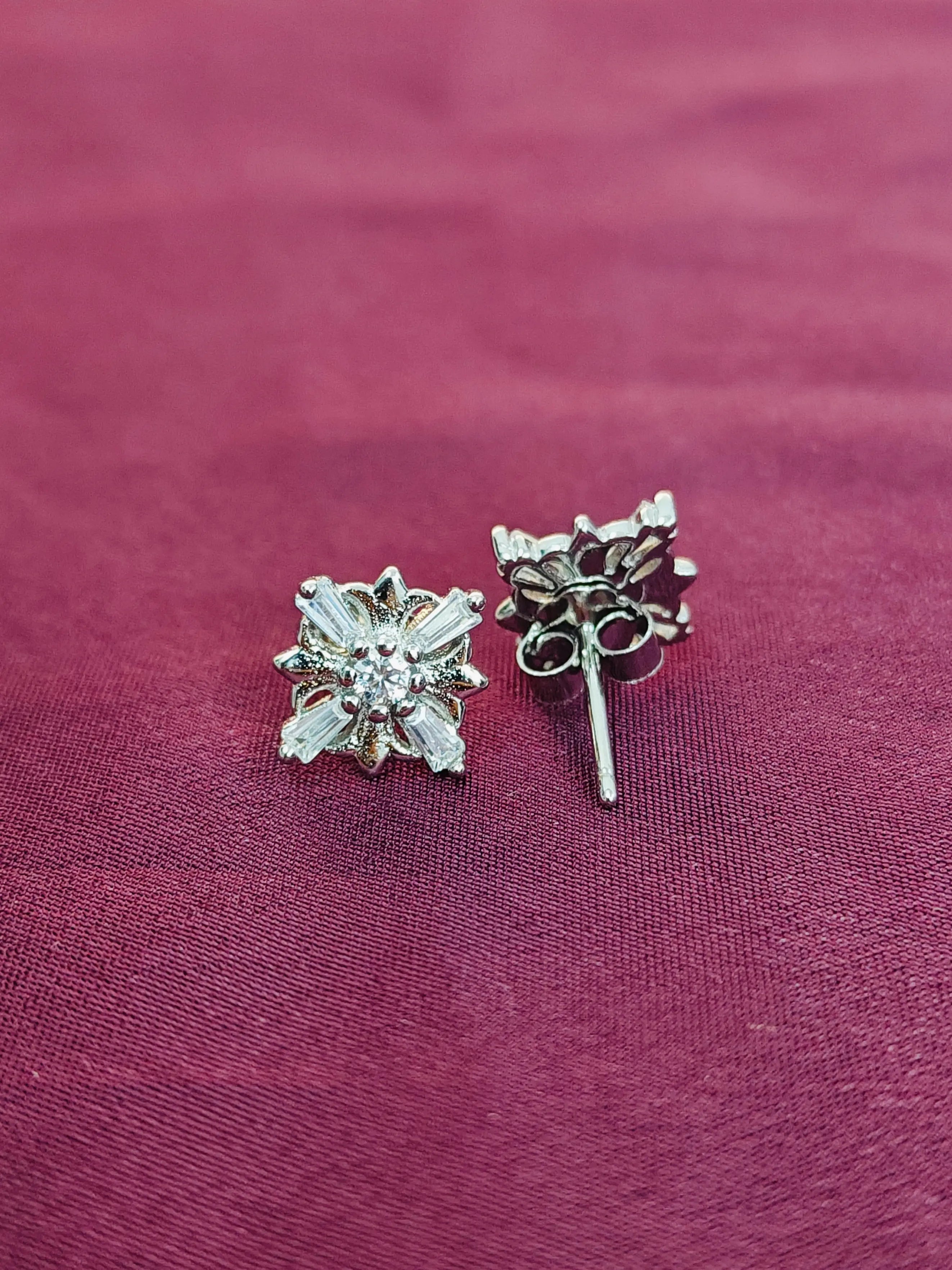 Silver floral earrings on a purple fabric background