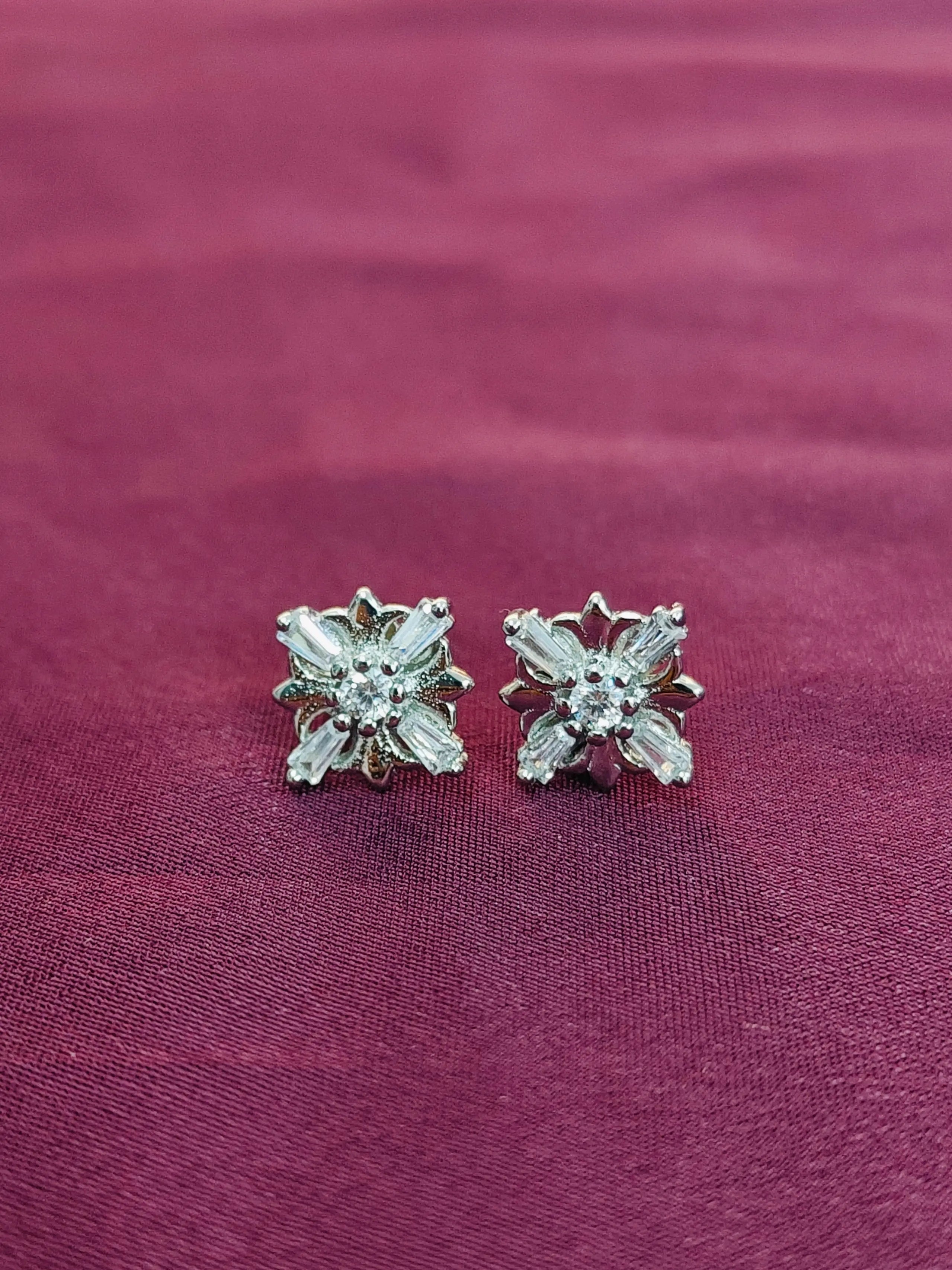 Pair of silver flower-shaped earrings on a purple fabric background
