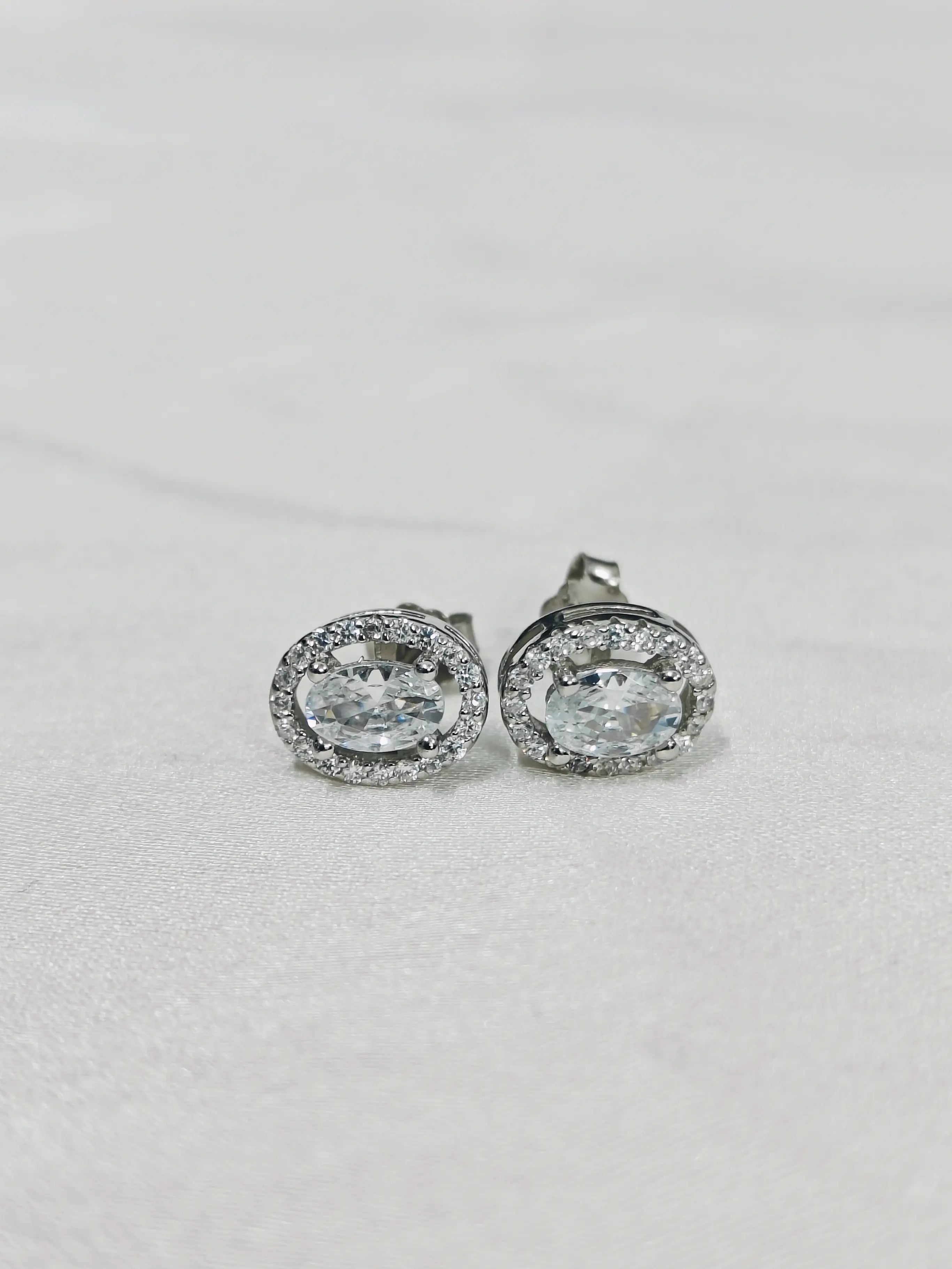 Pair of silver earrings with clear gemstones on a light gray background
