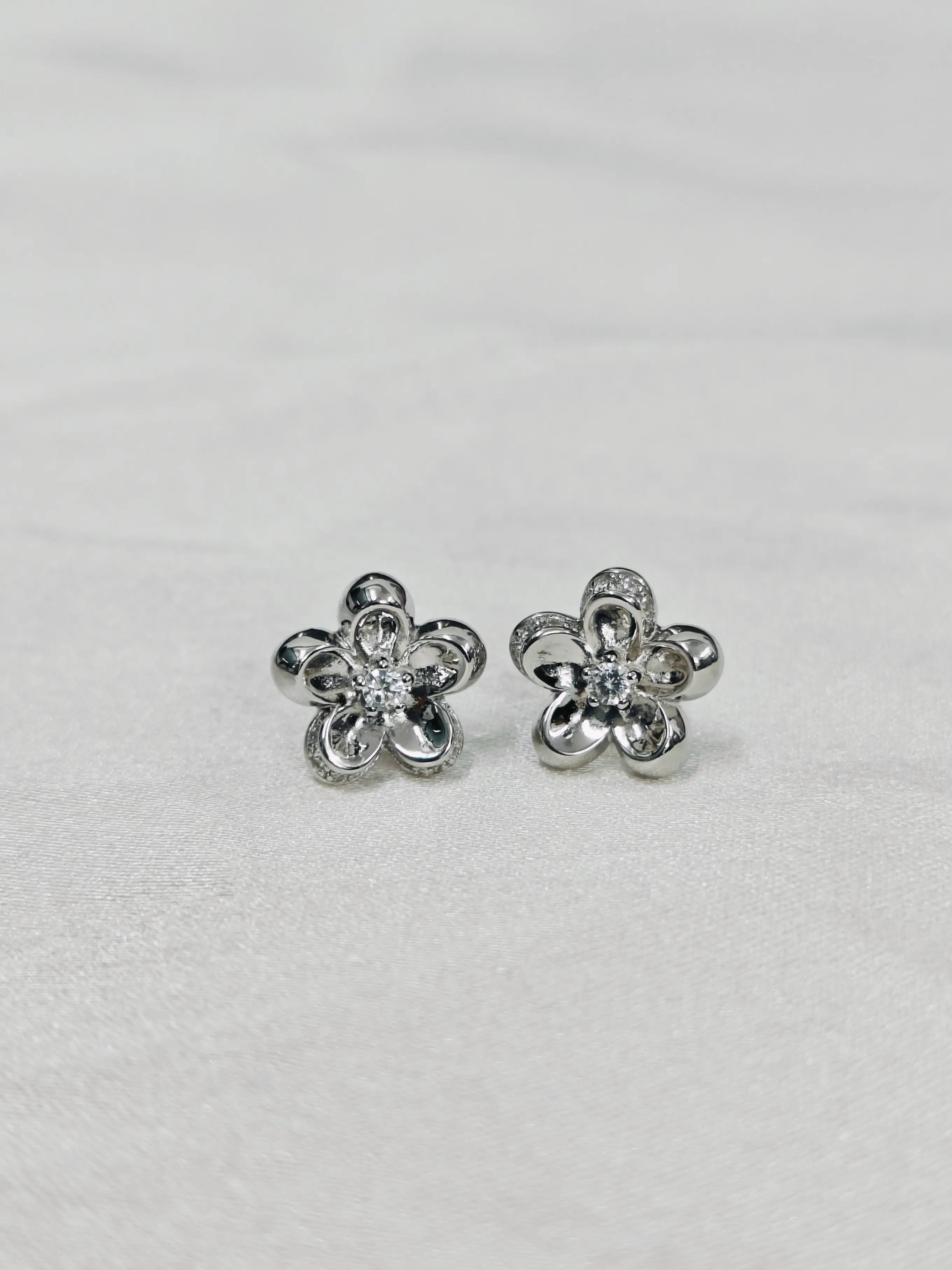 Flower-shaped silver earrings with clear stones on a light gray background