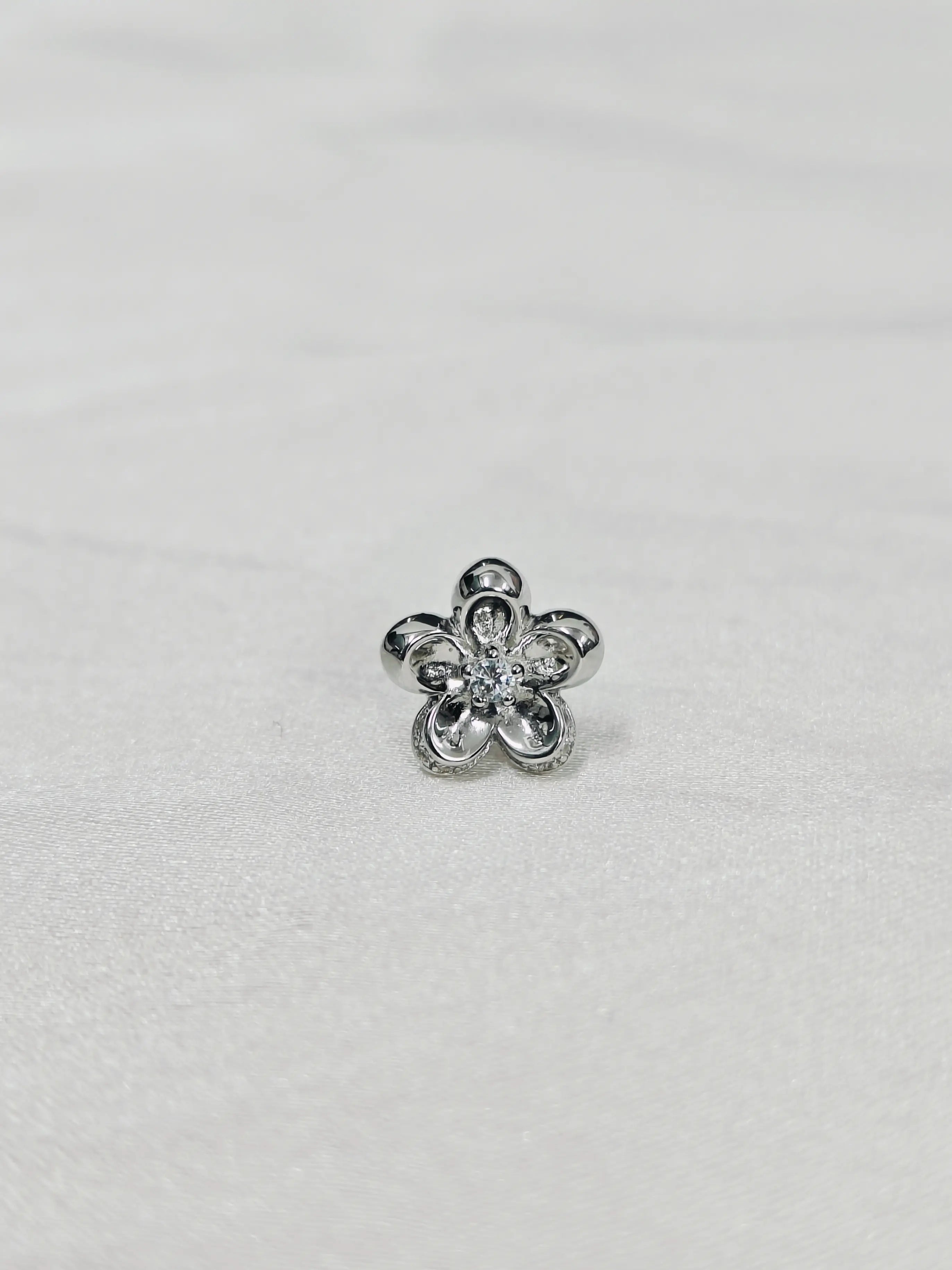 Silver flower-shaped earring on a light gray background