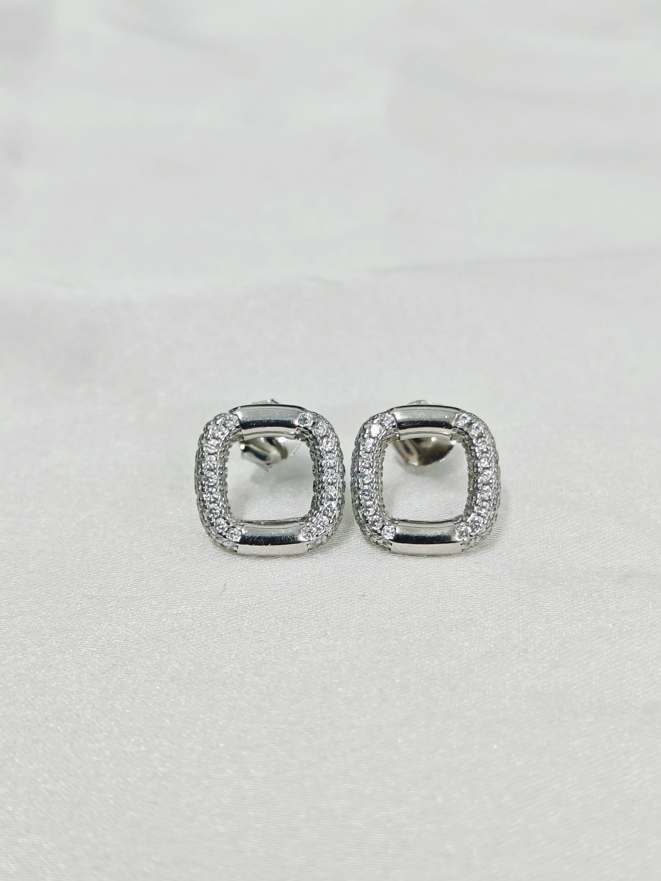 Pair of silver earrings with clear stones on a light gray background