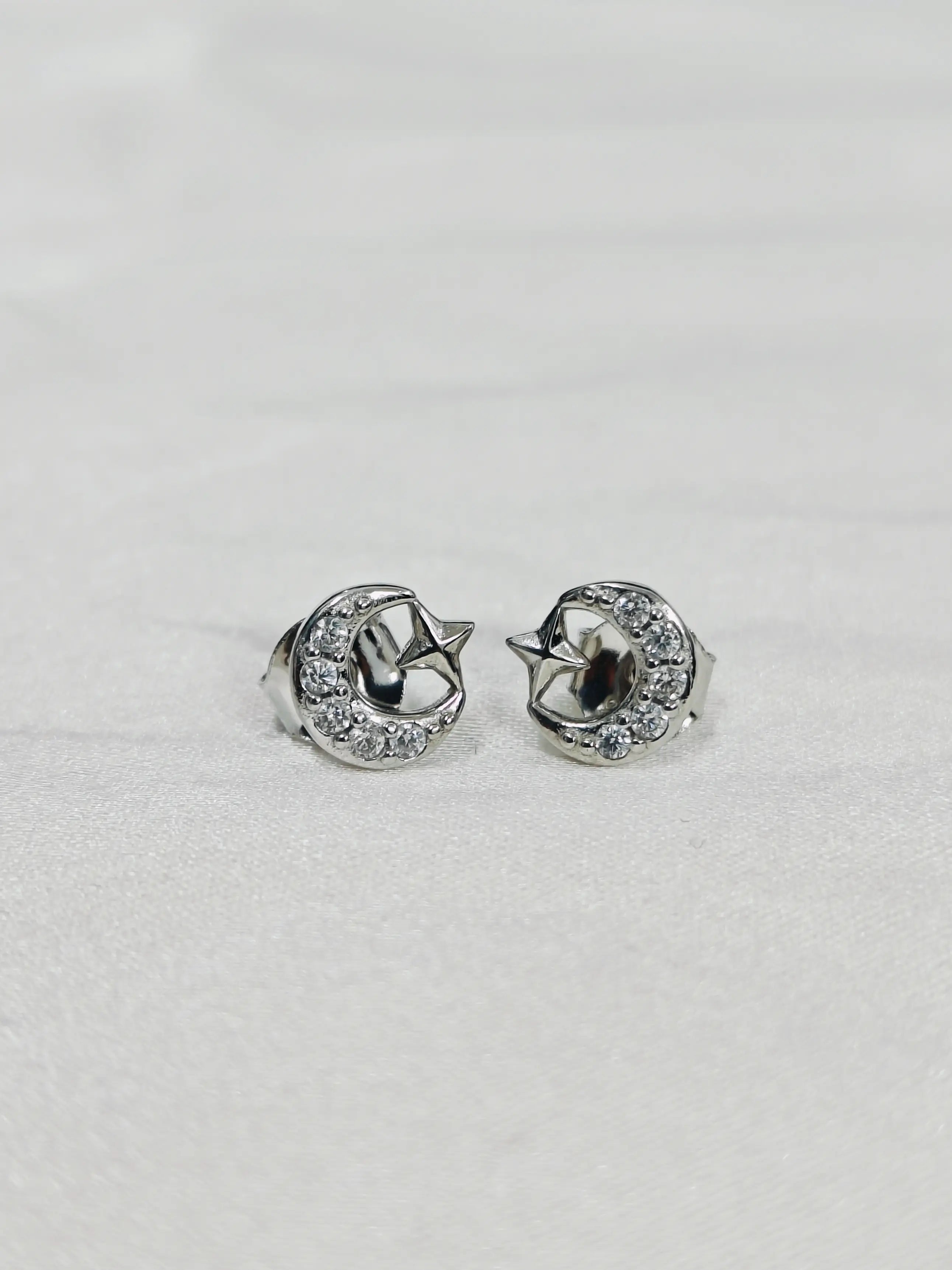 Pair of silver earrings with star and moon design on a light gray background