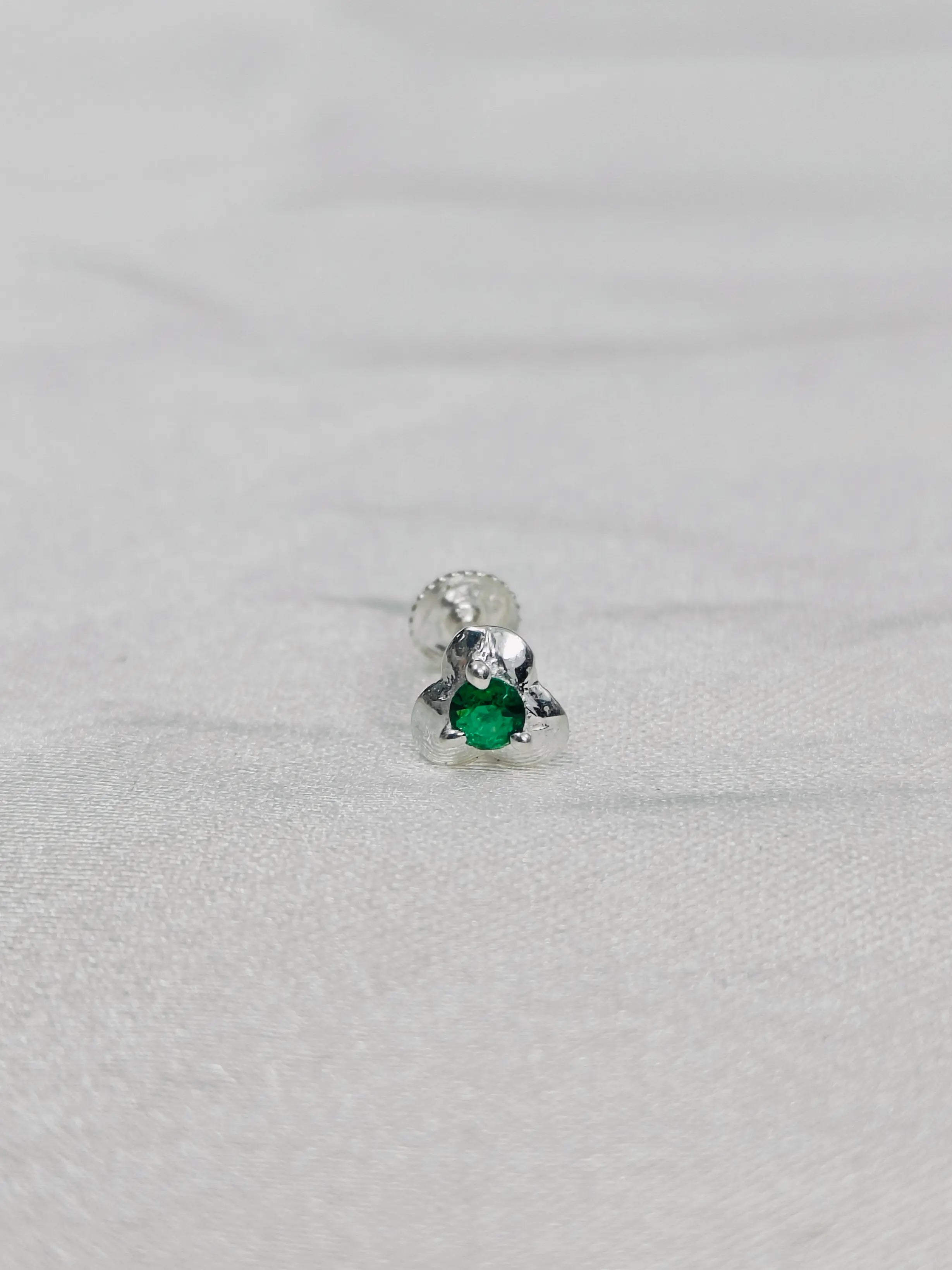 Silver earring with a green gemstone on a light gray background