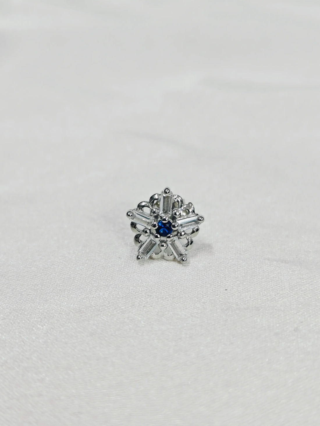 Silver earring with a blue gemstone on a white background
