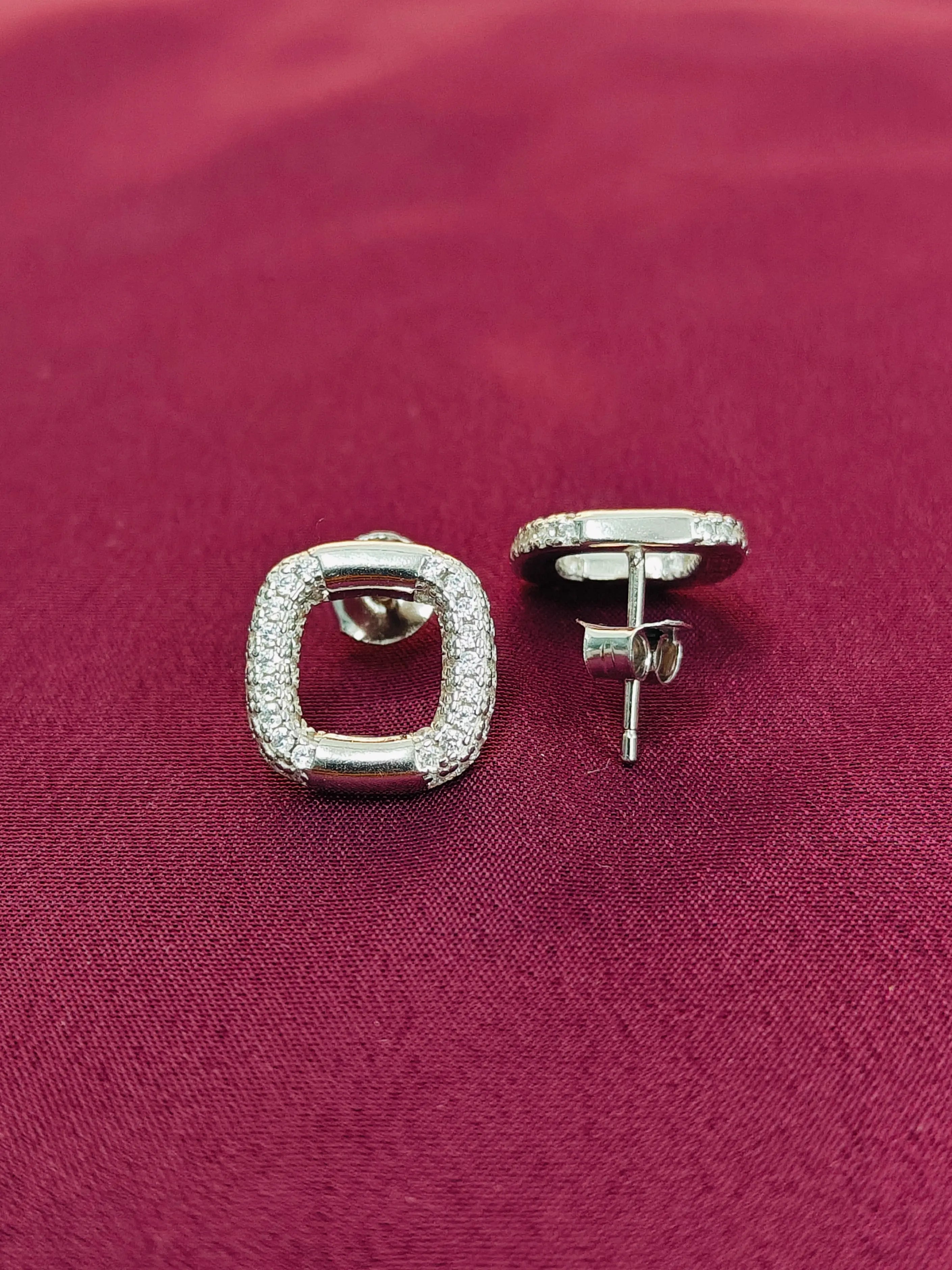 Silver square earrings with clear stones on a red fabric background