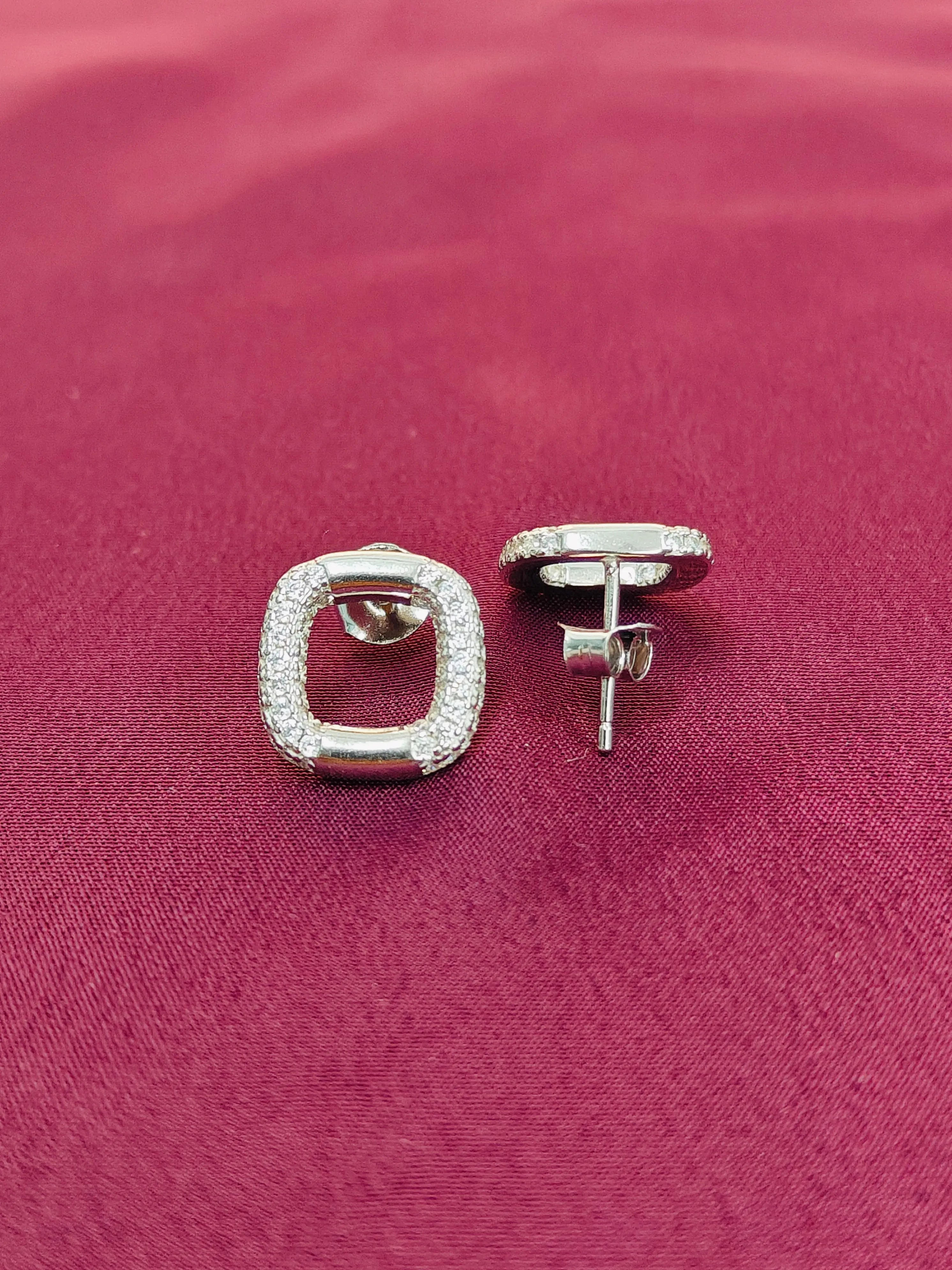 Silver square stud earrings on a pink fabric background