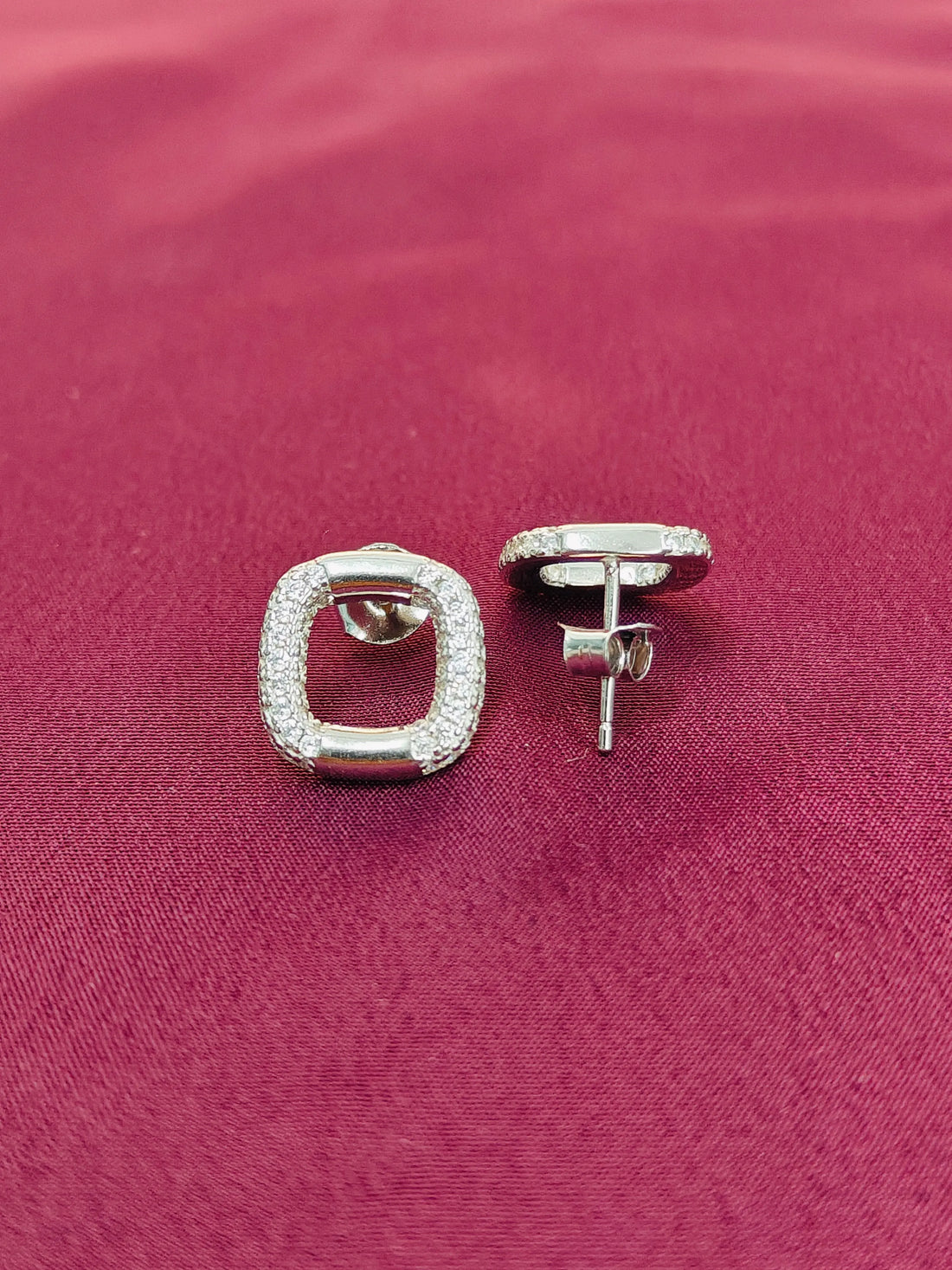 Silver square stud earrings on a pink fabric background