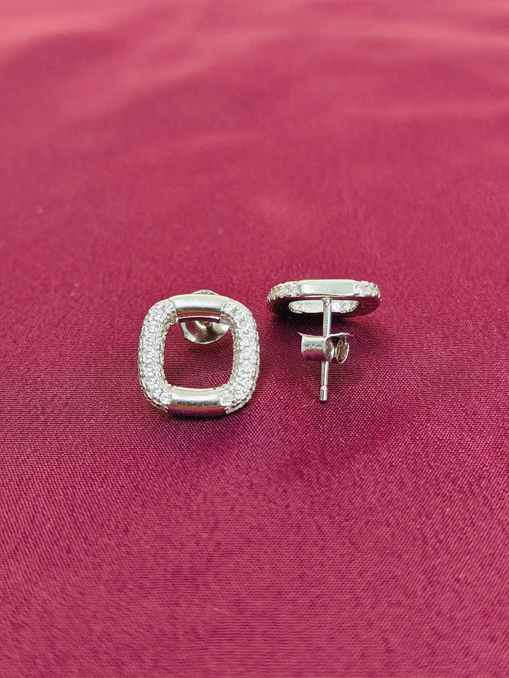 Silver square stud earrings on a pink fabric background