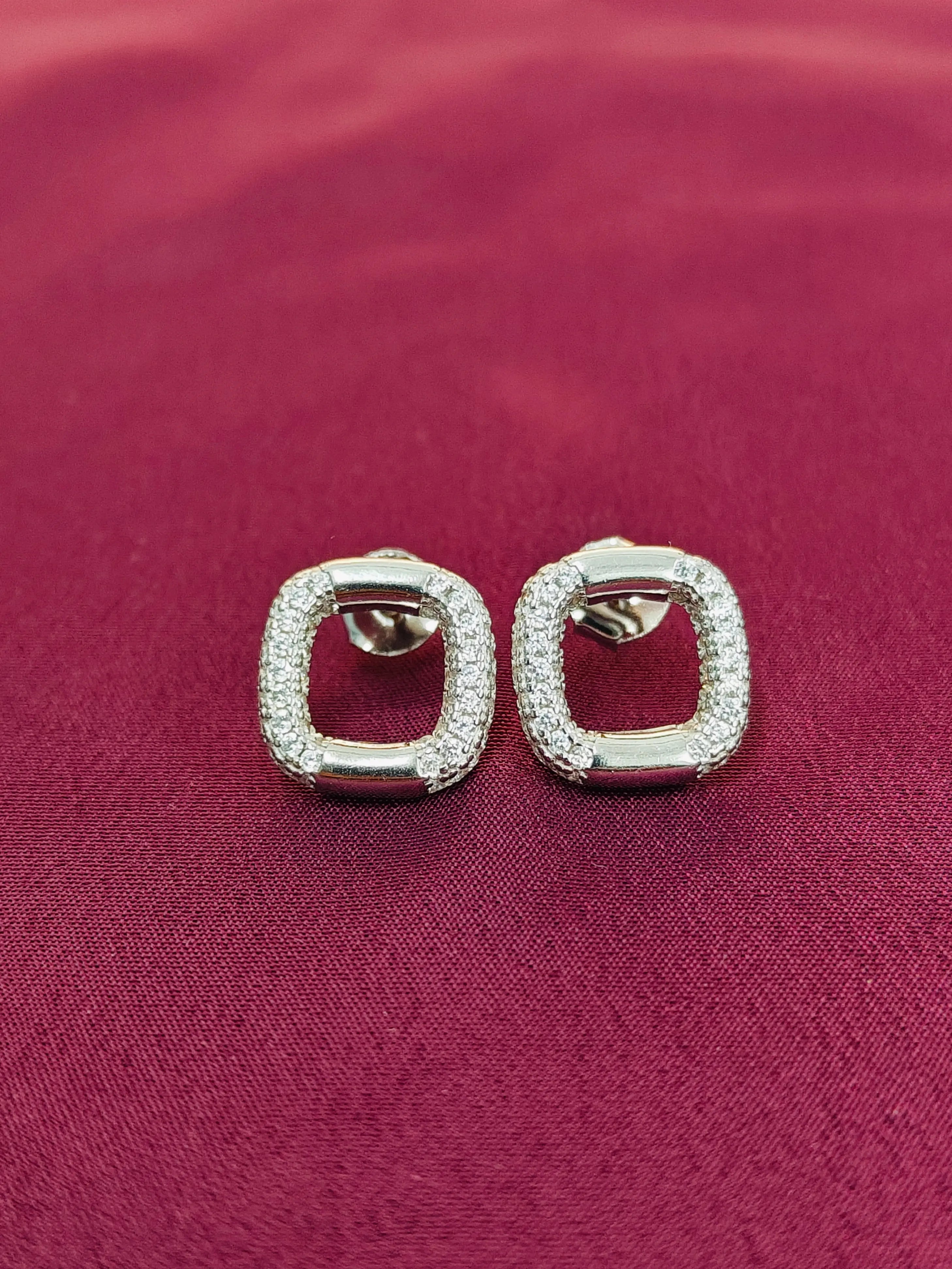 Pair of square-shaped earrings with clear stones on a red fabric background