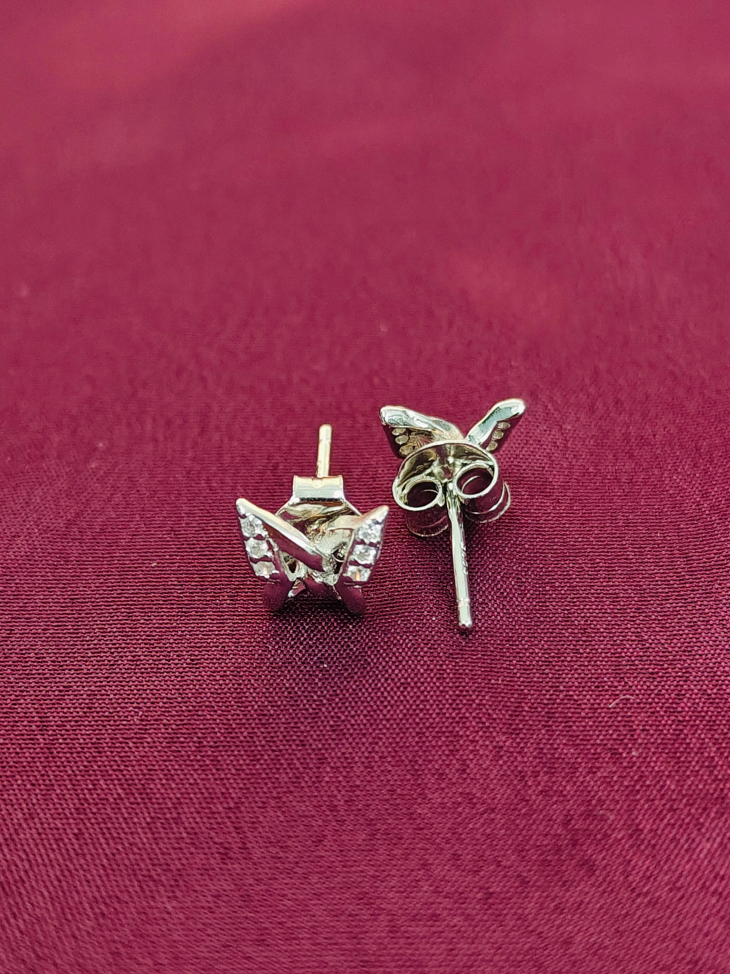Silver butterfly earrings on a maroon fabric background