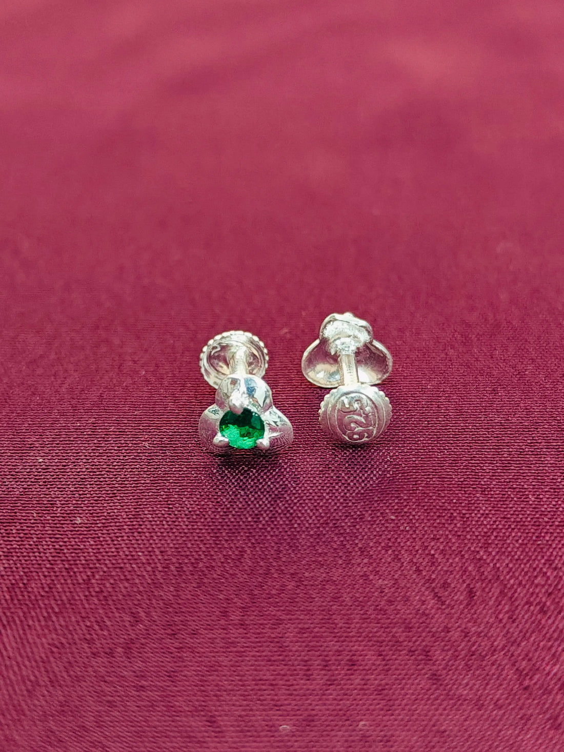 Silver earrings with a green gemstone on a red fabric background