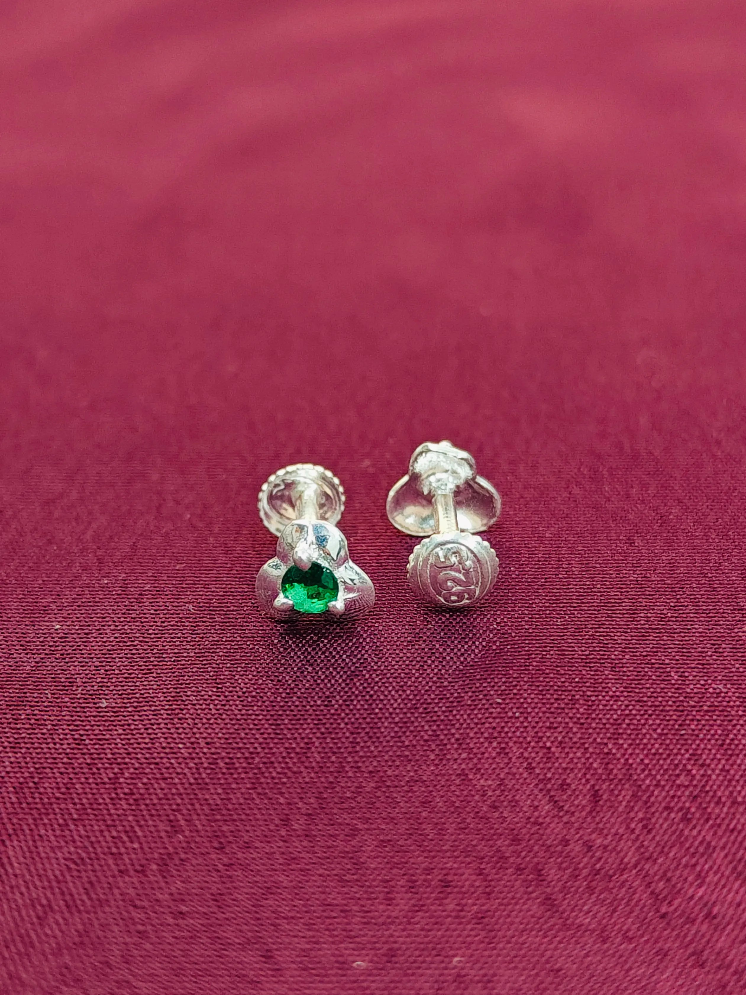 Silver earrings with a green gemstone on a red fabric background