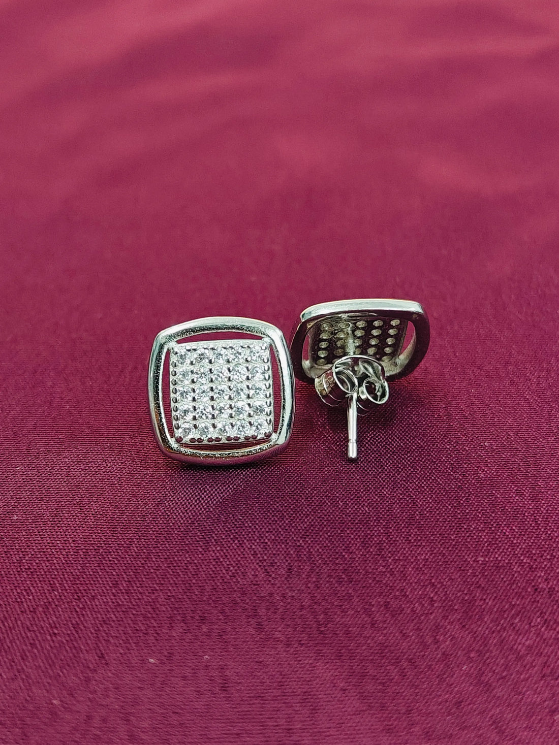 Silver square earrings with clear stones on a red fabric background