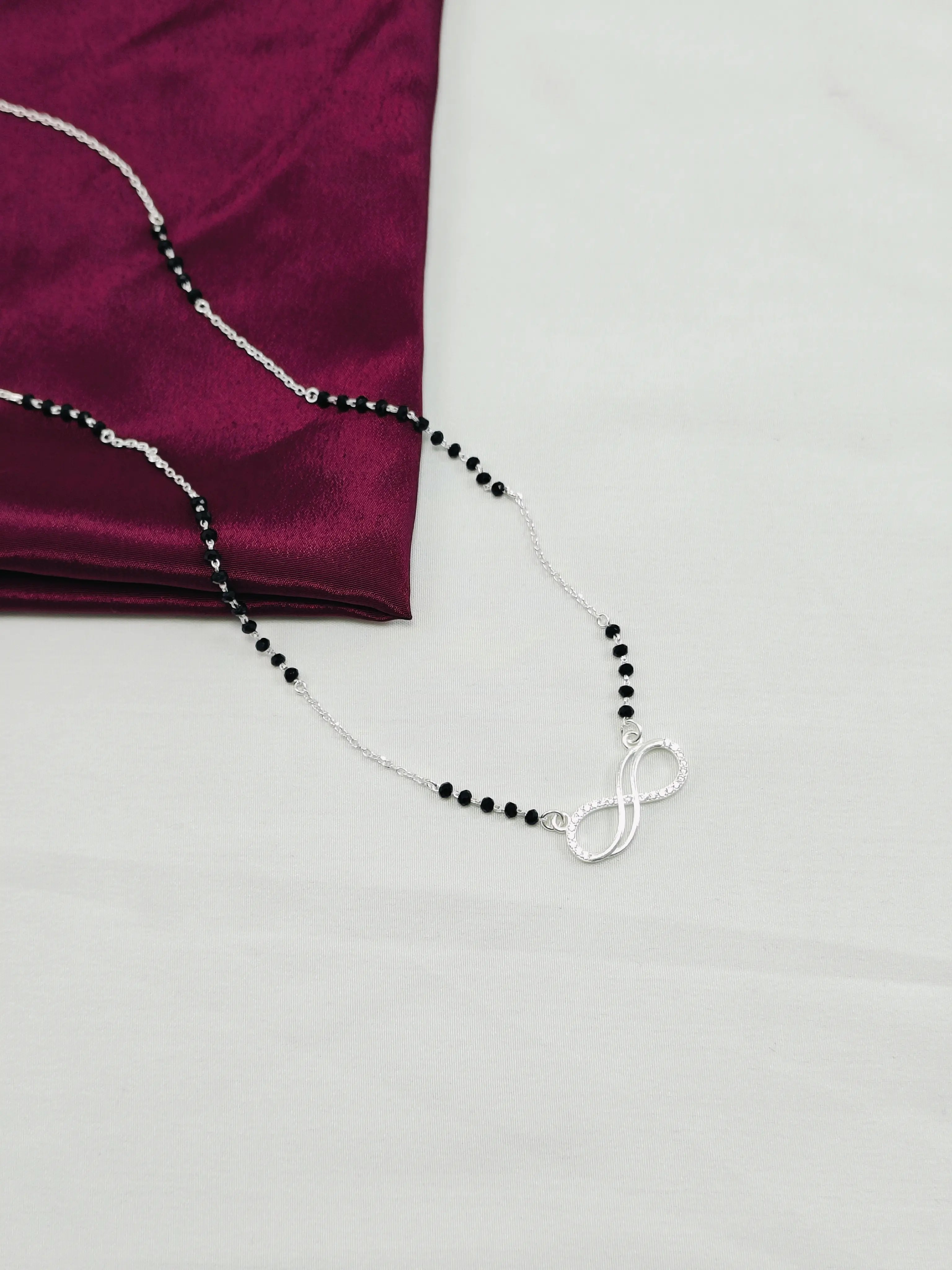 Necklace with black beads and silver infinity symbol on a purple fabric background