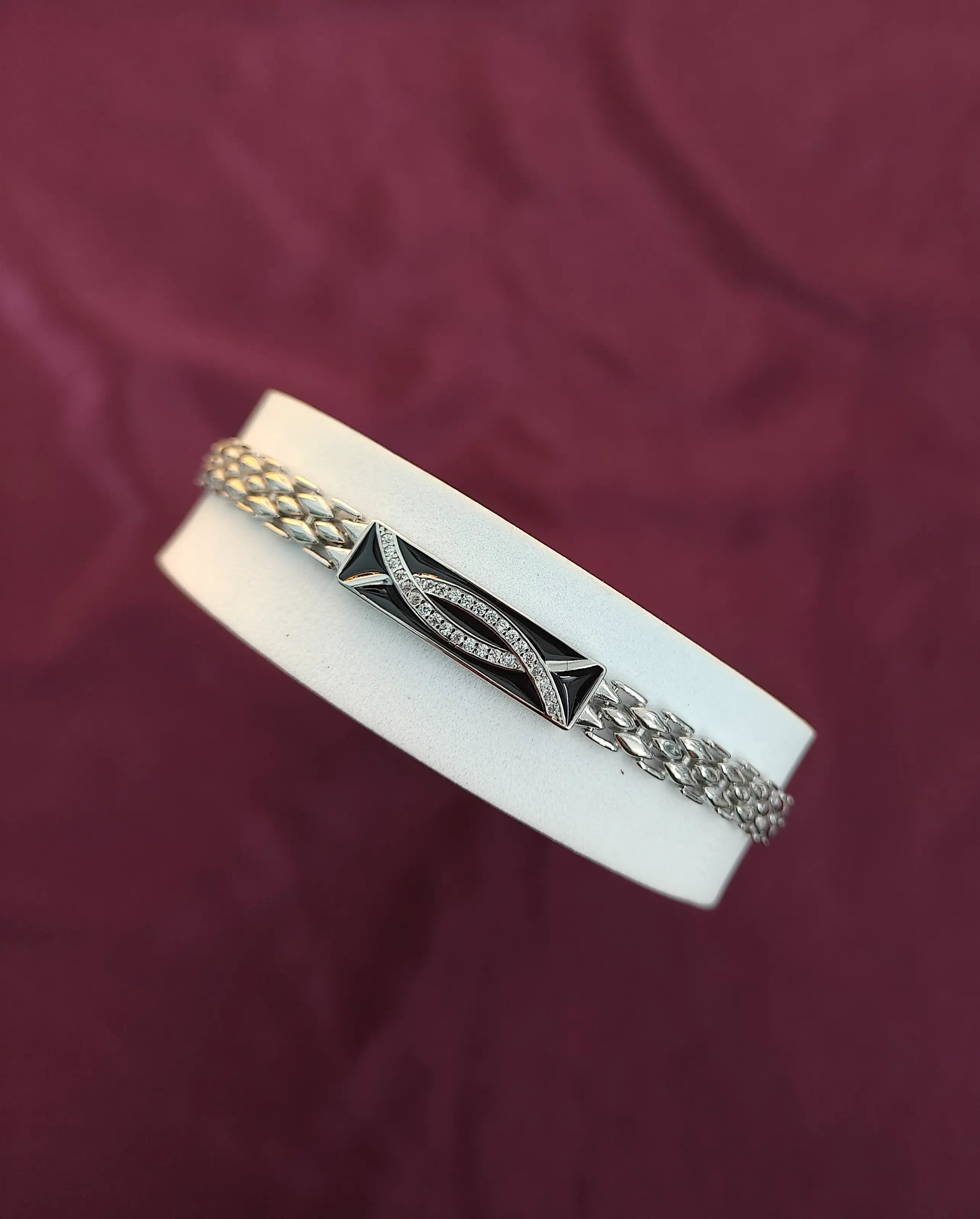 Silver bracelet with geometric design on a white stand against a maroon background