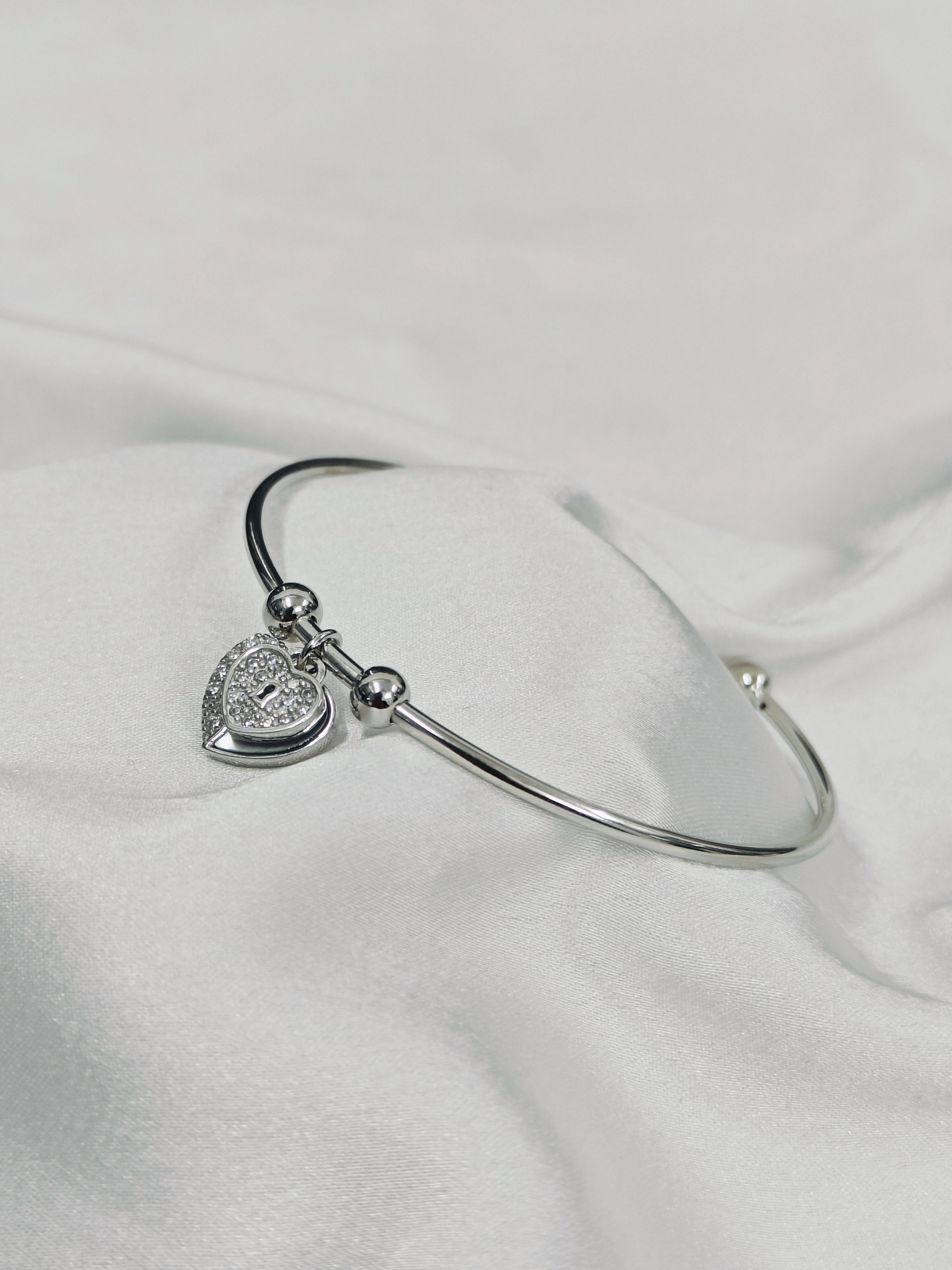 Silver bracelet with a heart-shaped charm on a white fabric background