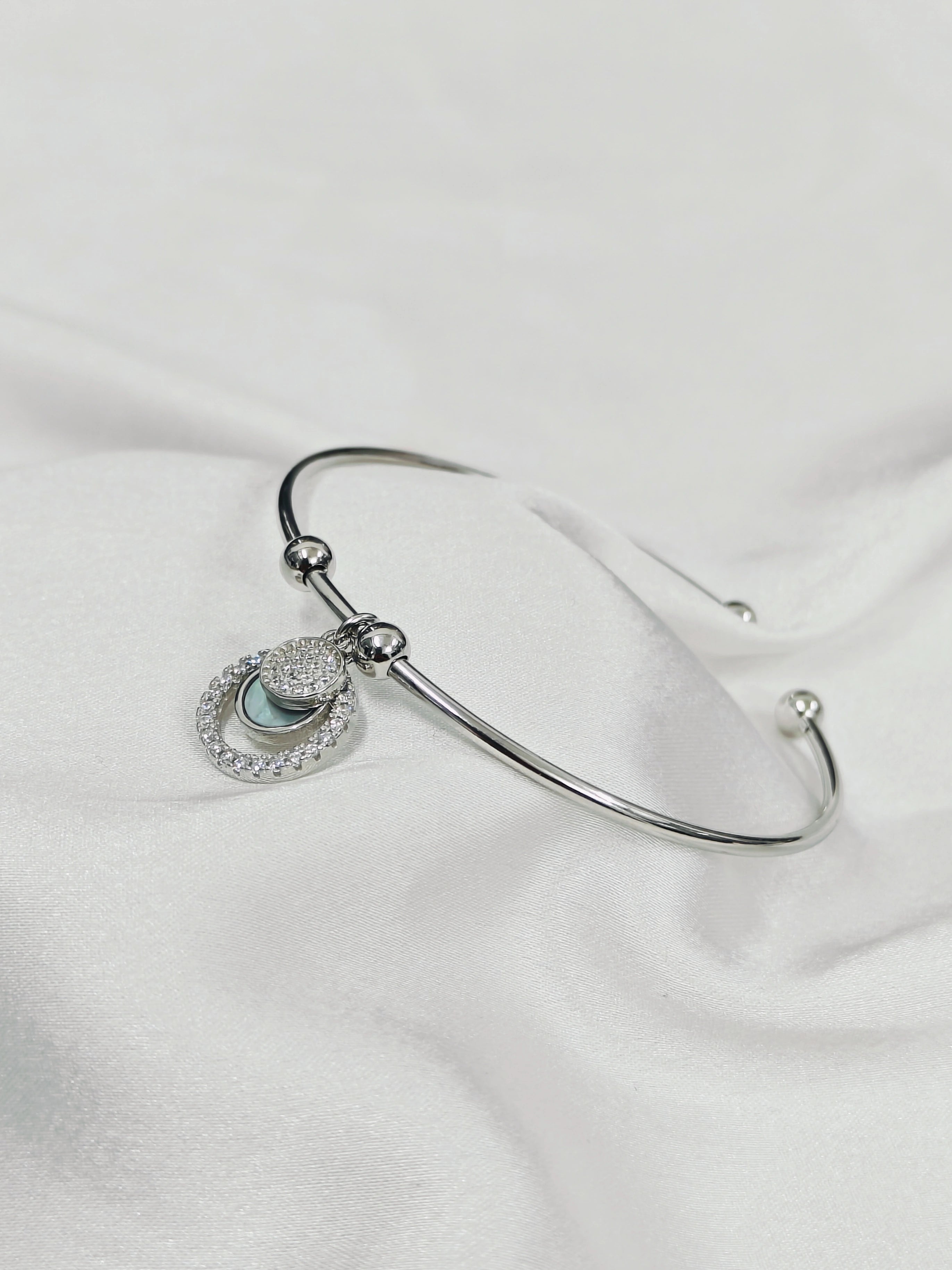Silver bracelet with a heart-shaped charm on a white fabric background