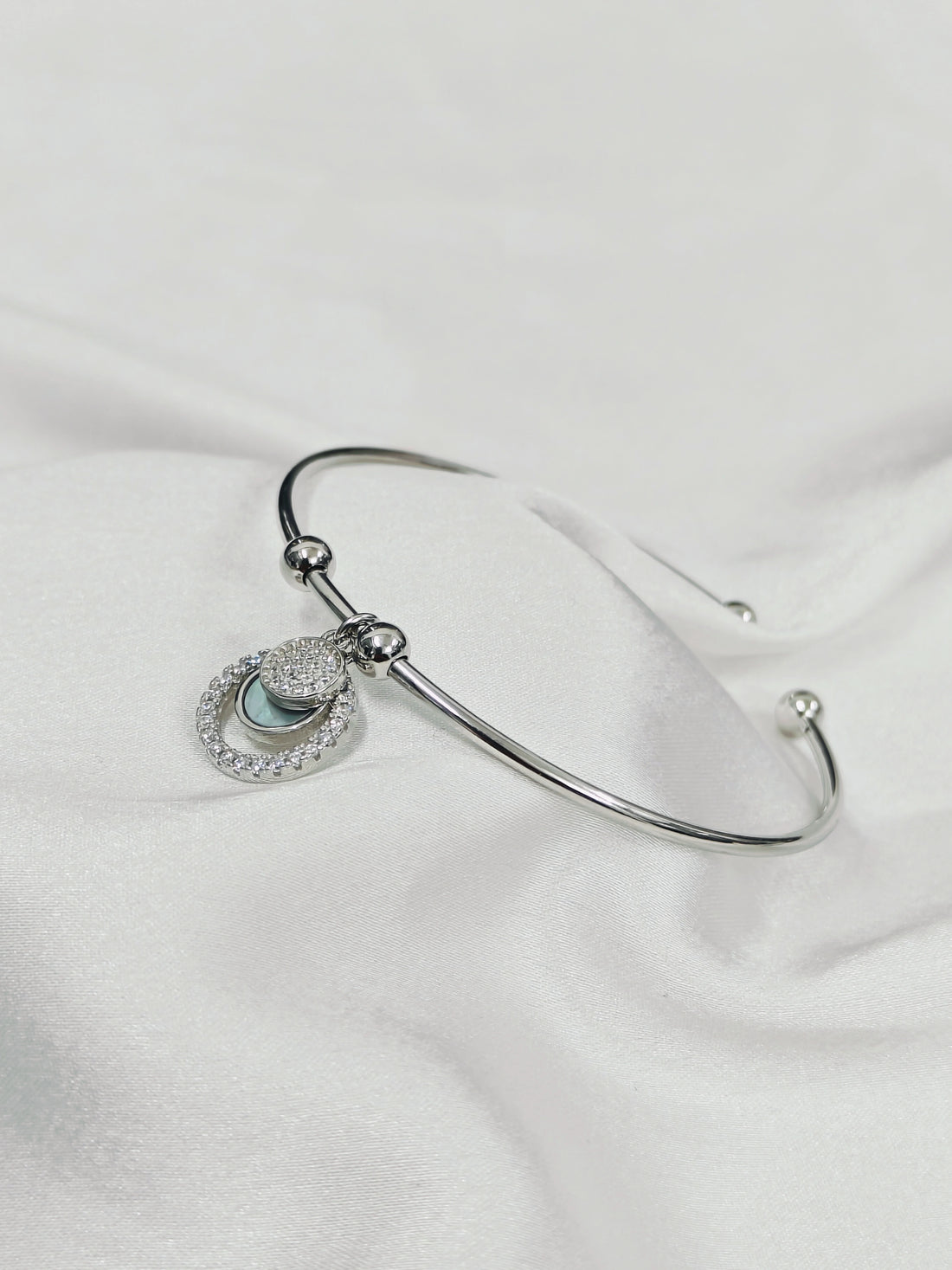 Silver bracelet with a heart-shaped charm on a white fabric background