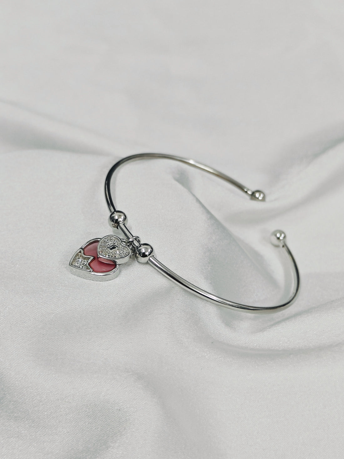 Silver bracelet with a heart-shaped charm on a white fabric background