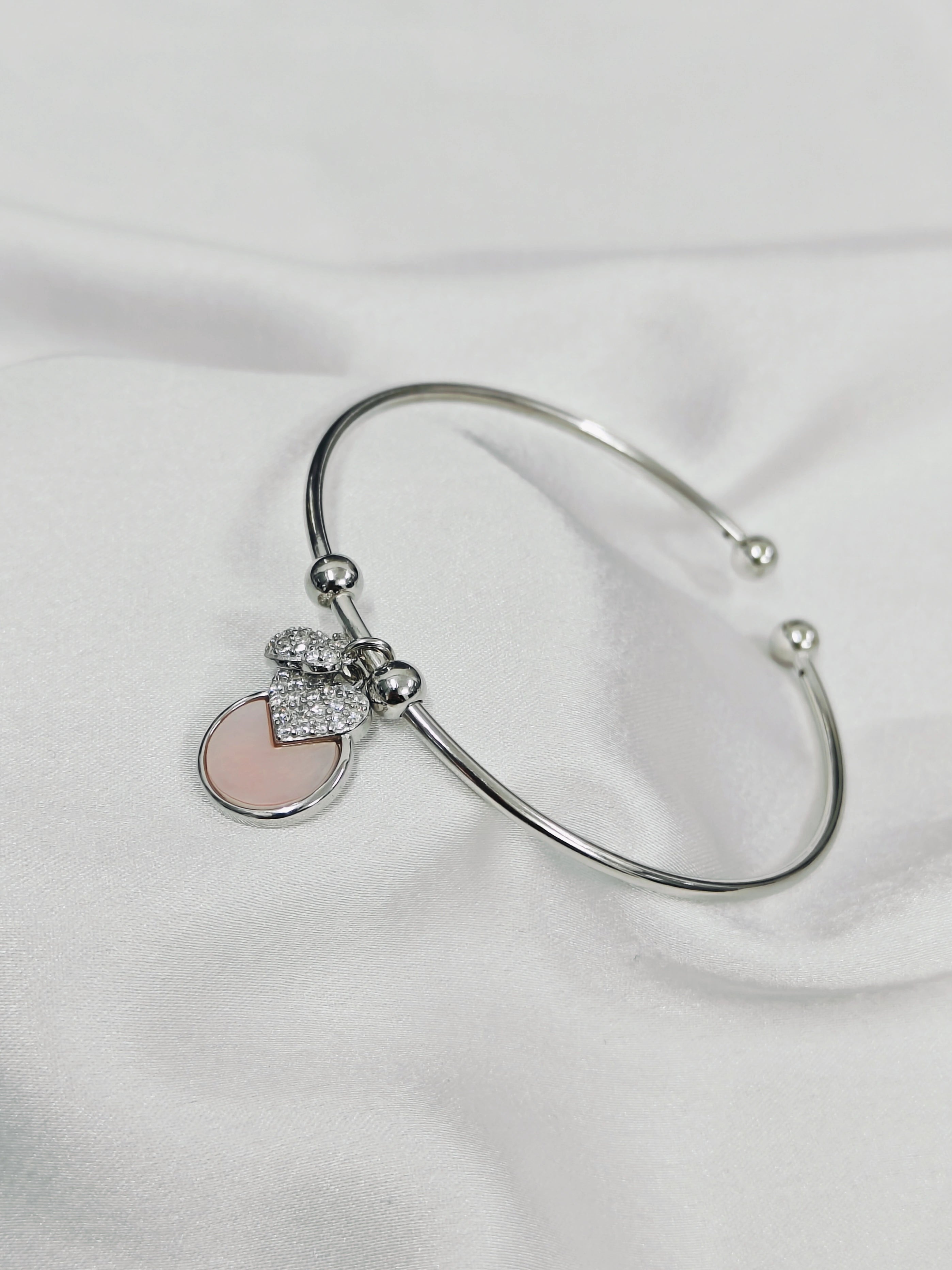 Silver bracelet with a heart-shaped charm on a white fabric background